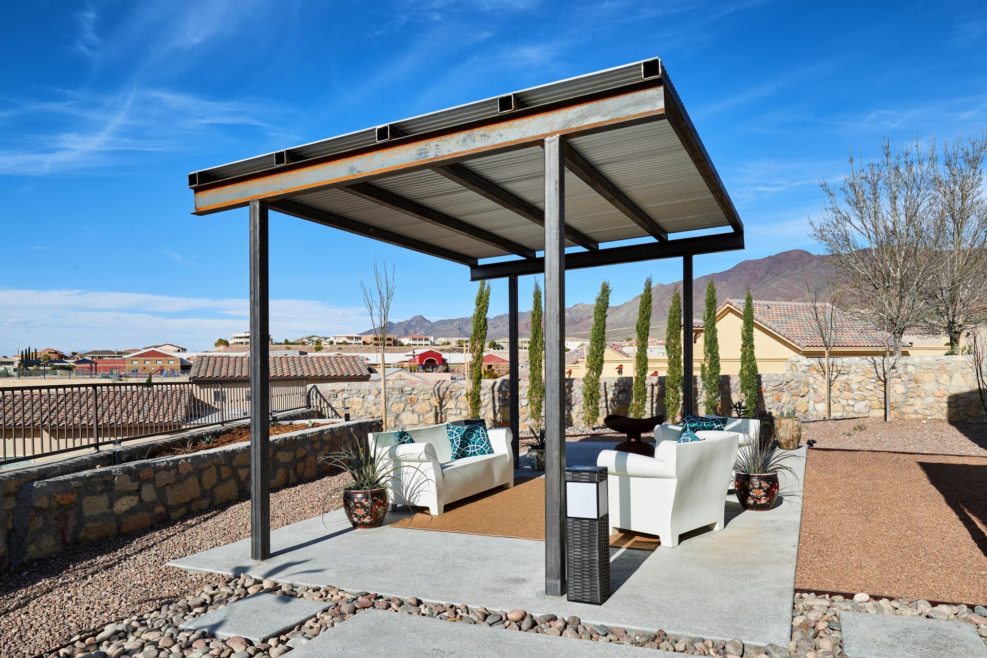 A covered outdoor seating area with white couches and a corrugated metal roof, on a sunny day.