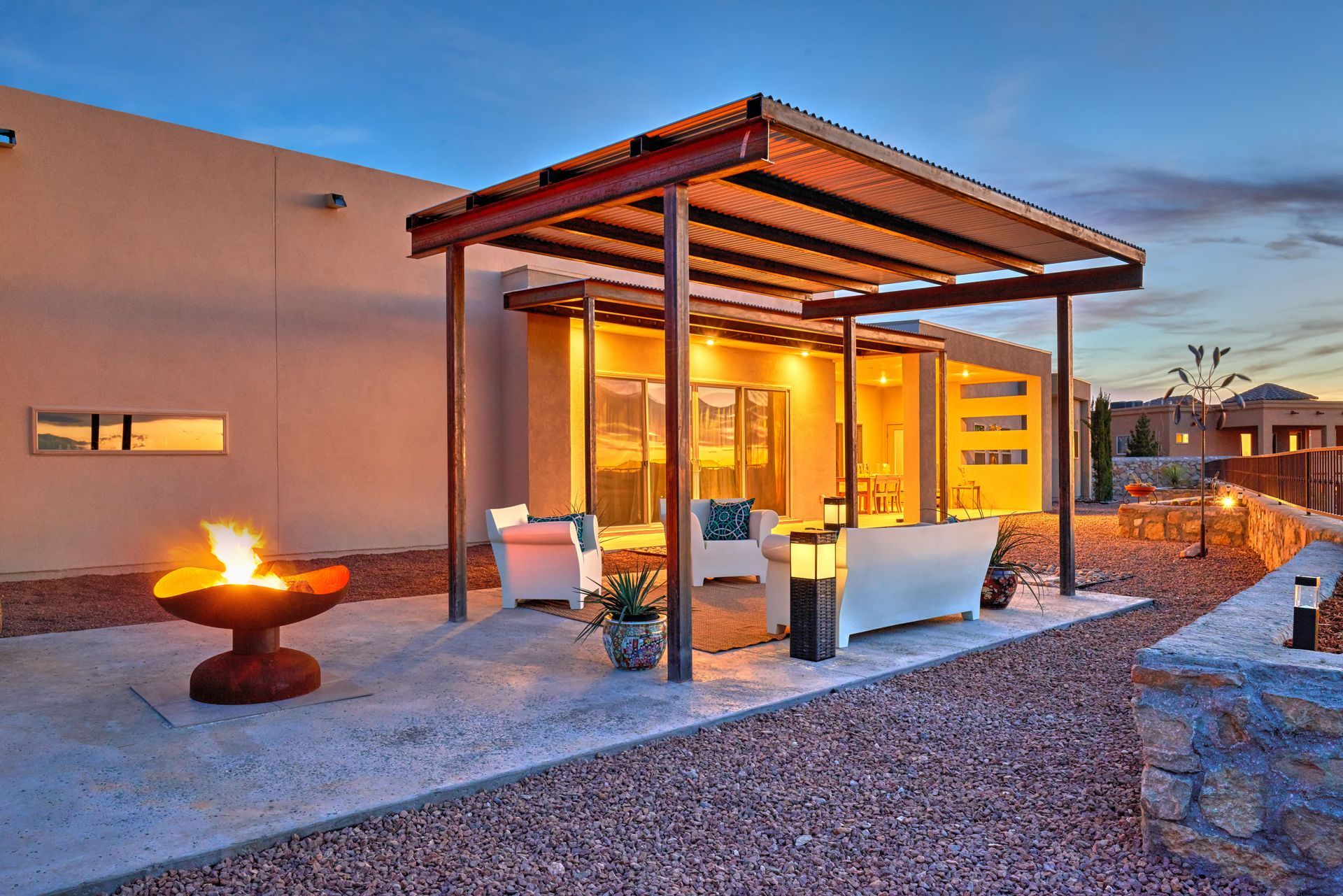 Outdoor patio with a fire pit, seating, and a covered area, set against a twilight sky.