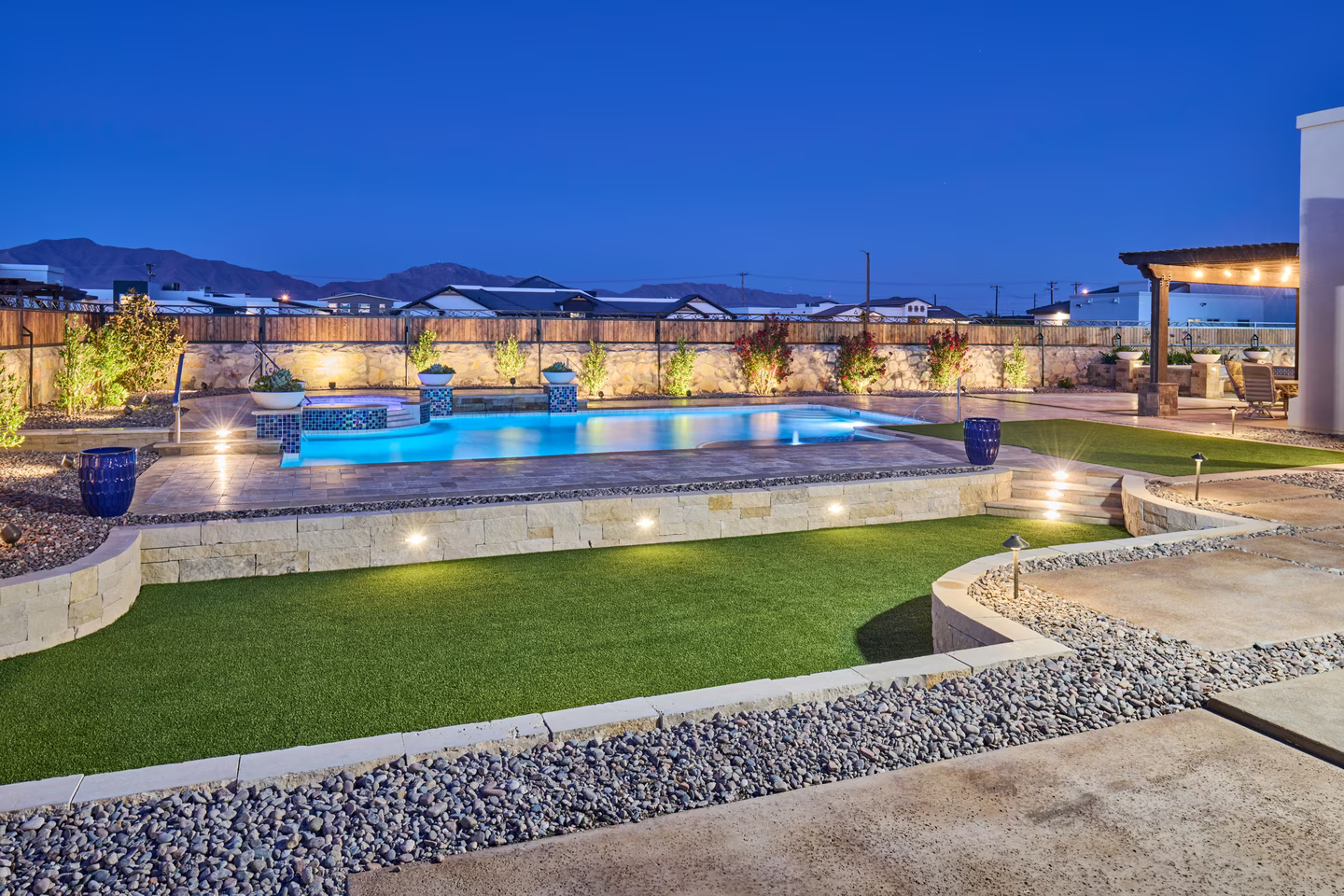 Backyard with pool and landscaping lit up at dusk.