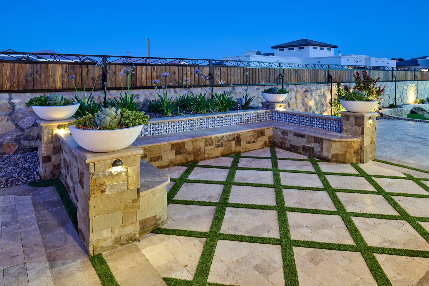 Stone bench with succulents and square patio with grass, under evening sky.