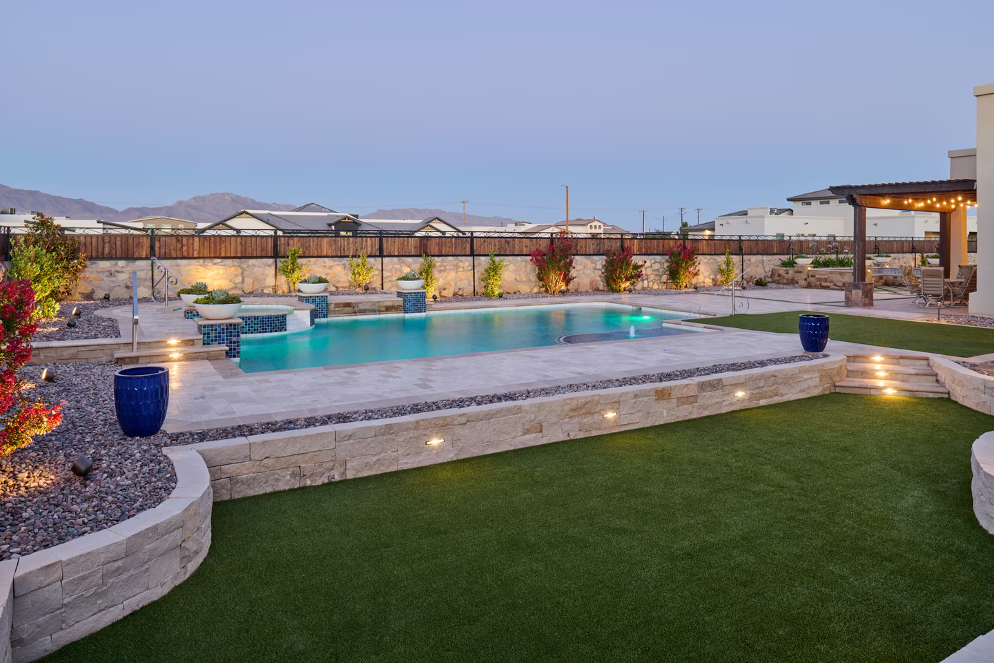 Backyard with a swimming pool, stone retaining walls, green grass, and mountains in the distance.
