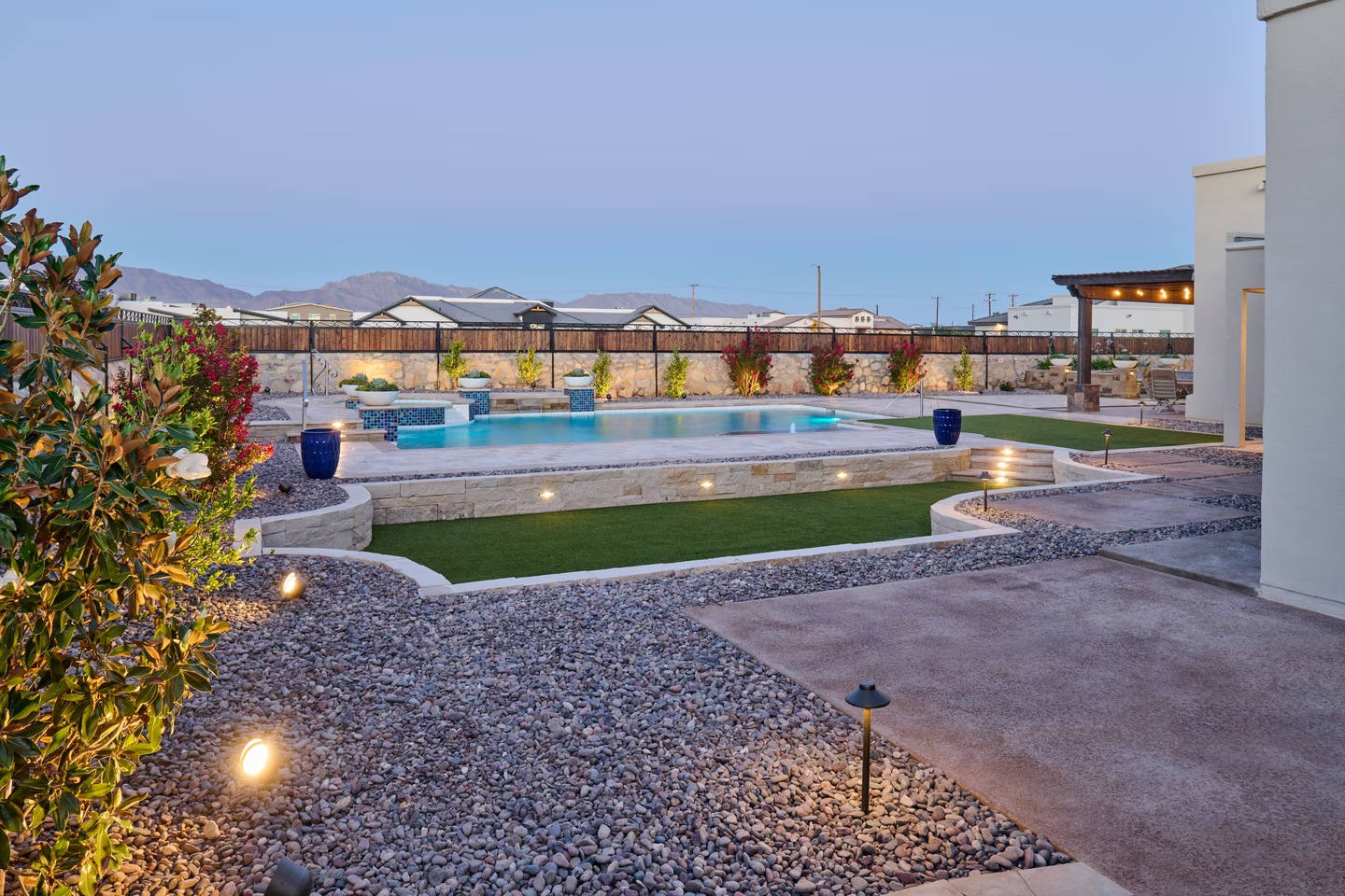 Backyard pool area at dusk with pool, landscaping, and pathway lighting. Mountains in background.