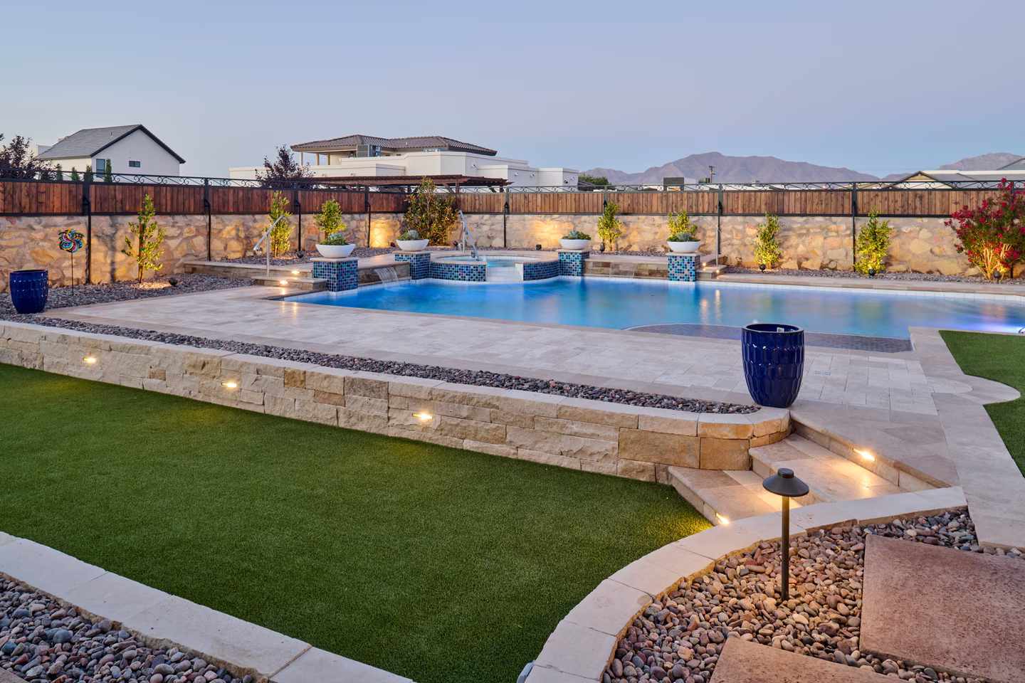 Pool with stone edging, water features, and landscaping at dusk.