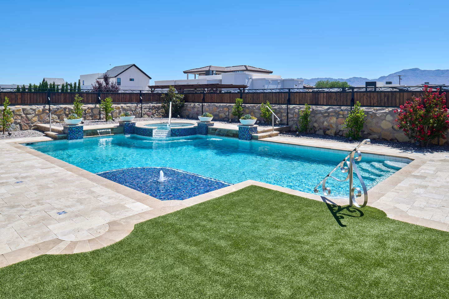 Swimming pool with turquoise water, waterfall feature, stone deck, and artificial grass lawn. Sunny, outdoor setting.