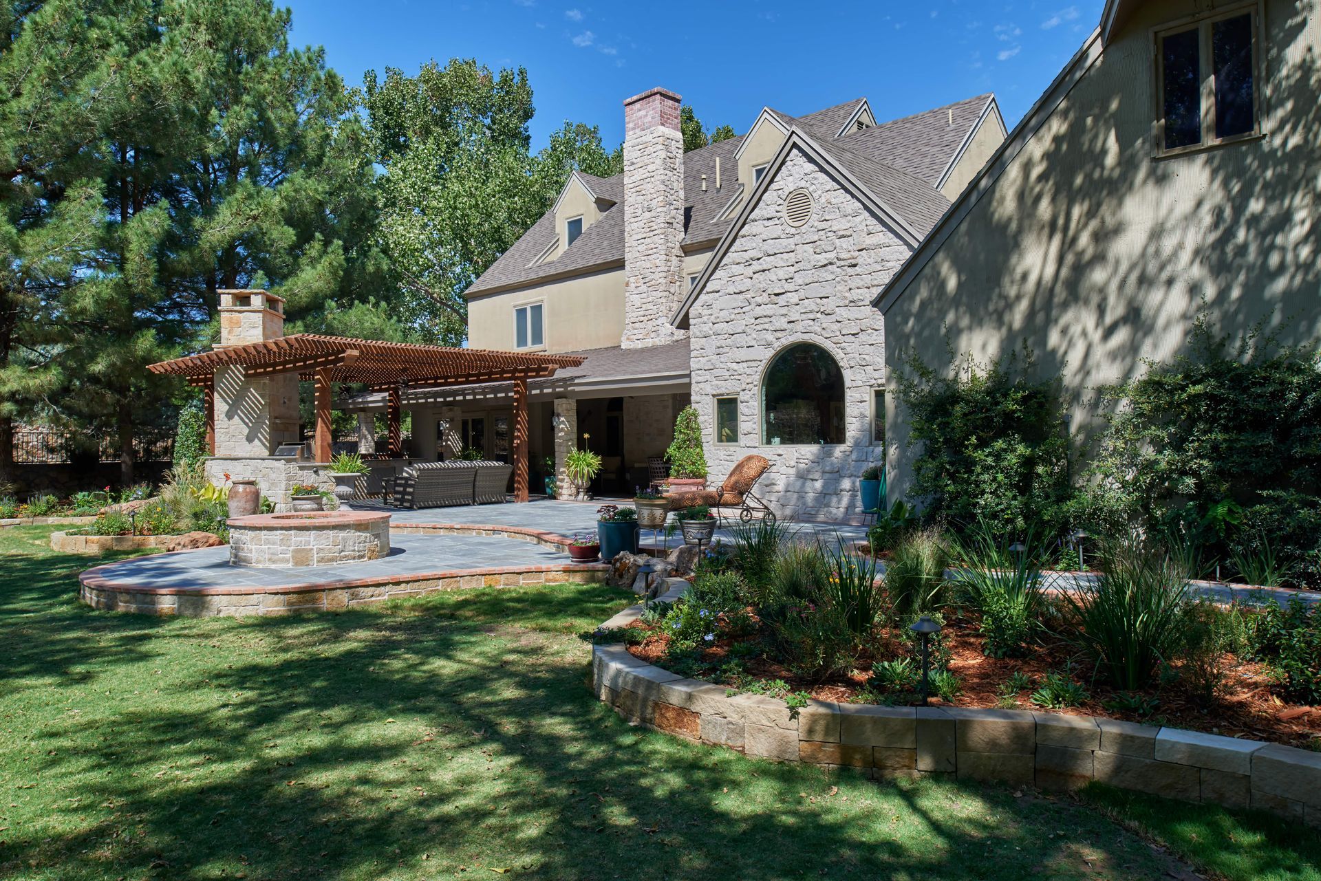 Backyard patio with stone, pergola, and house with brick exterior.
