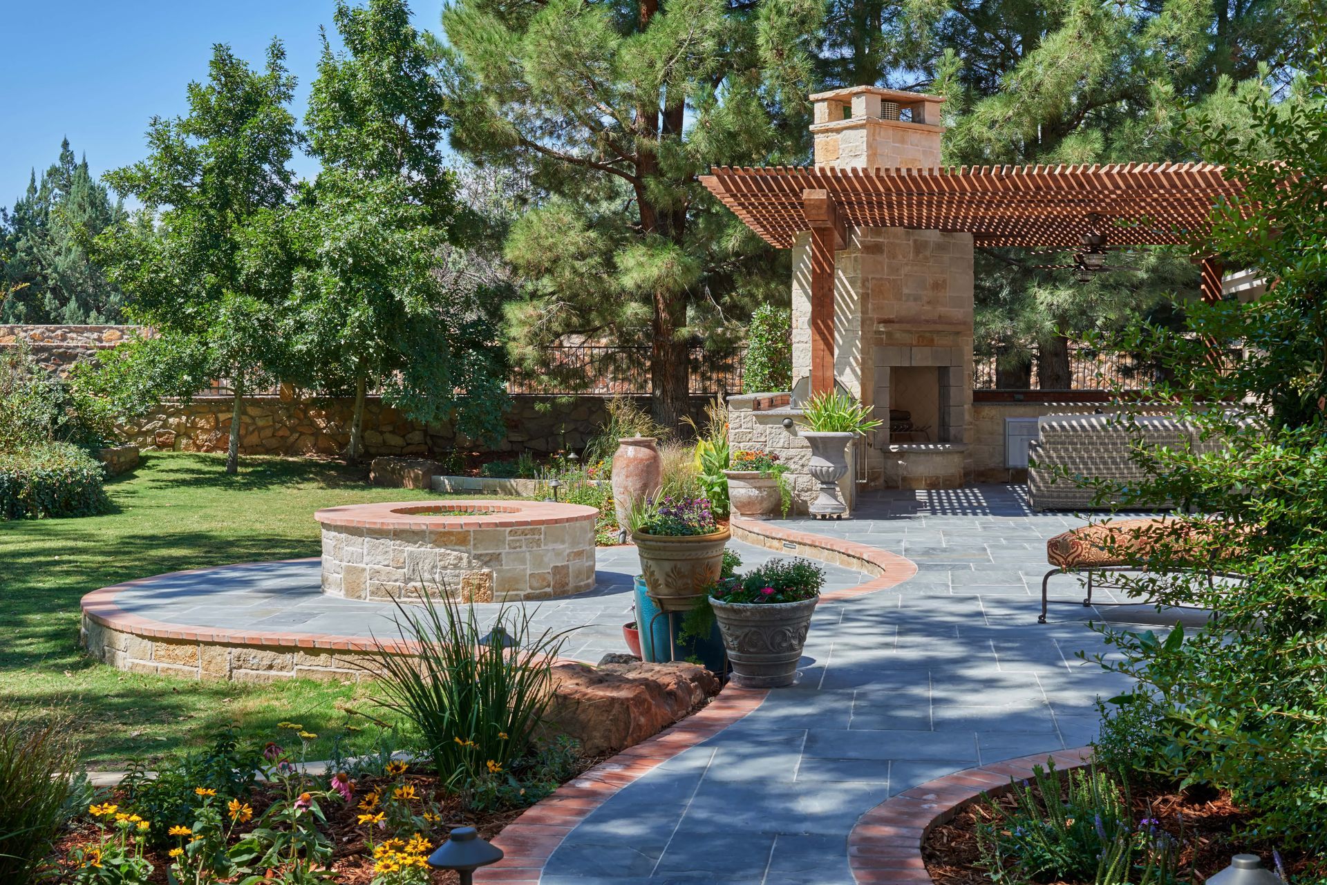 Outdoor patio with fireplace, fire pit, and pergola; trees and landscaping surround.