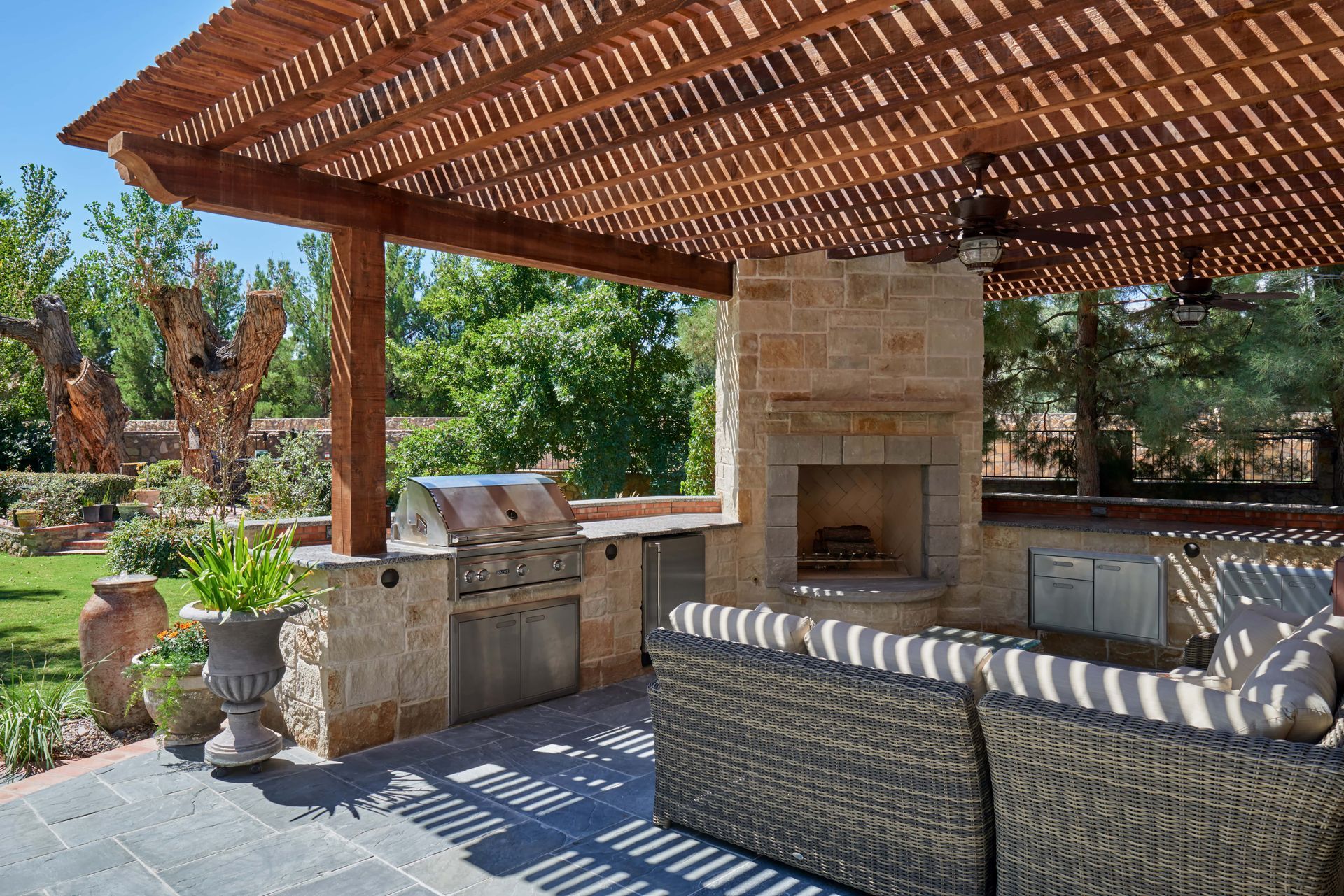 Outdoor kitchen with a grill, fireplace, and seating under a wood pergola.