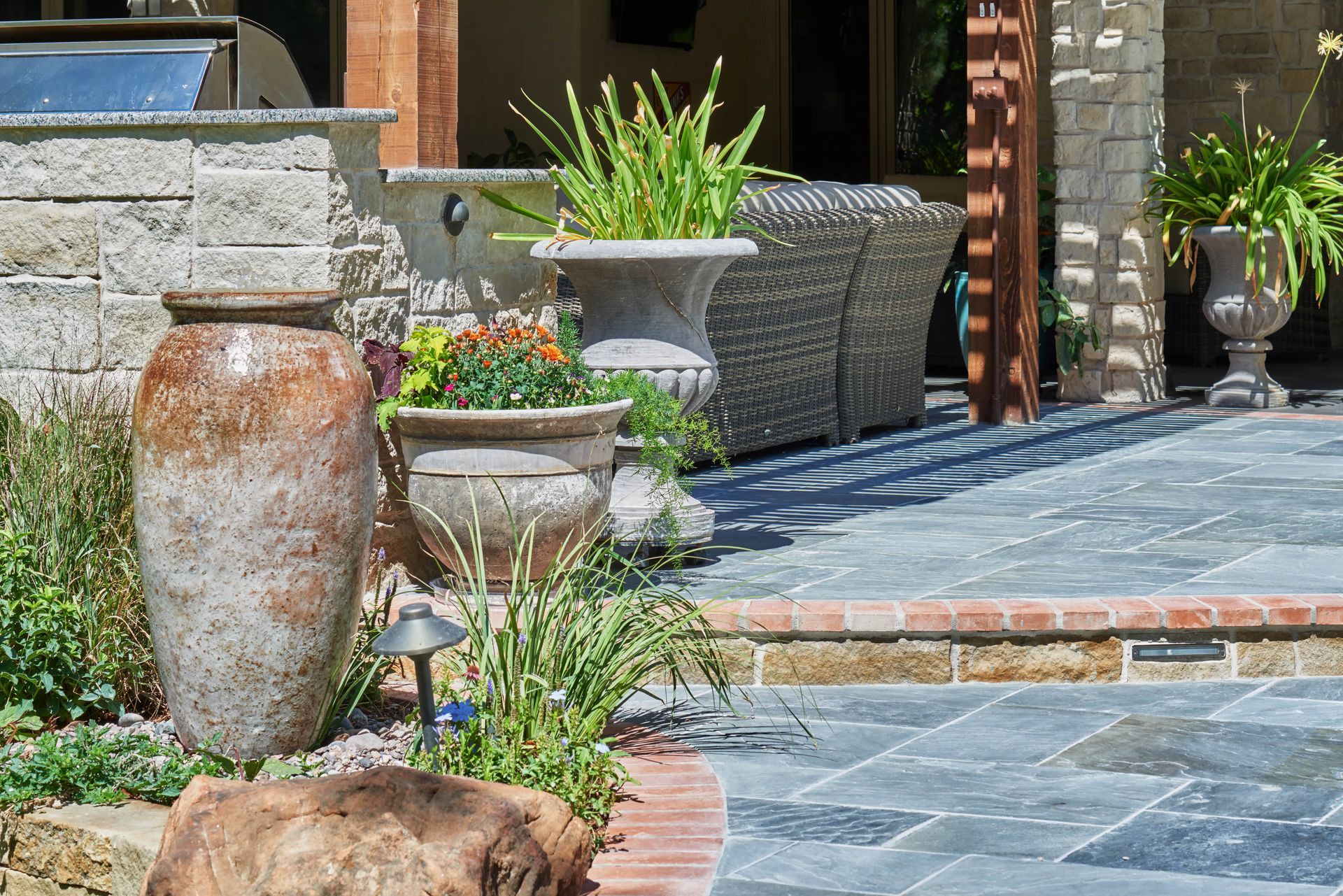 Outdoor patio with stone pavers, large pottery, and potted plants.