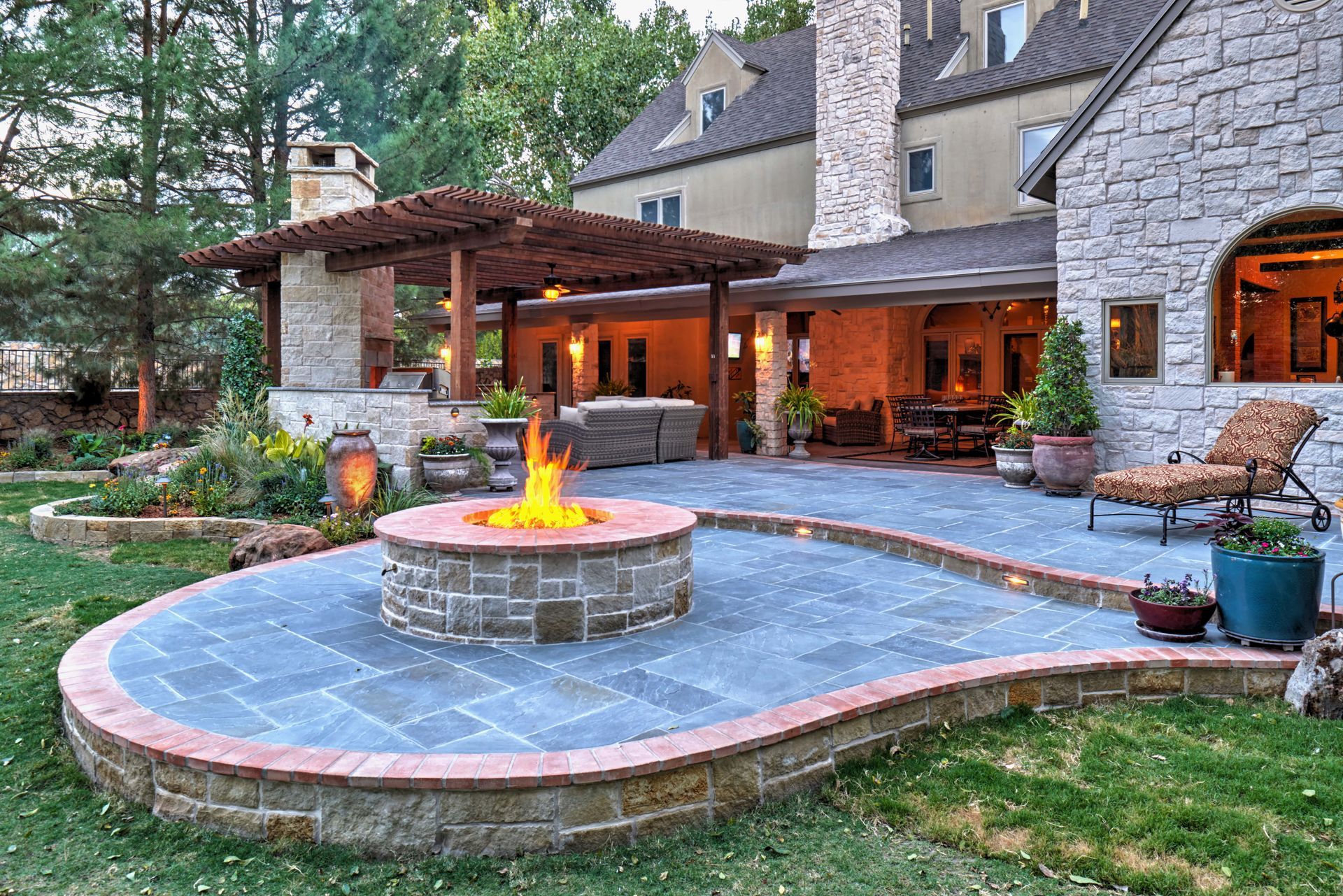Stone patio with fire pit, pergola, and house exterior.