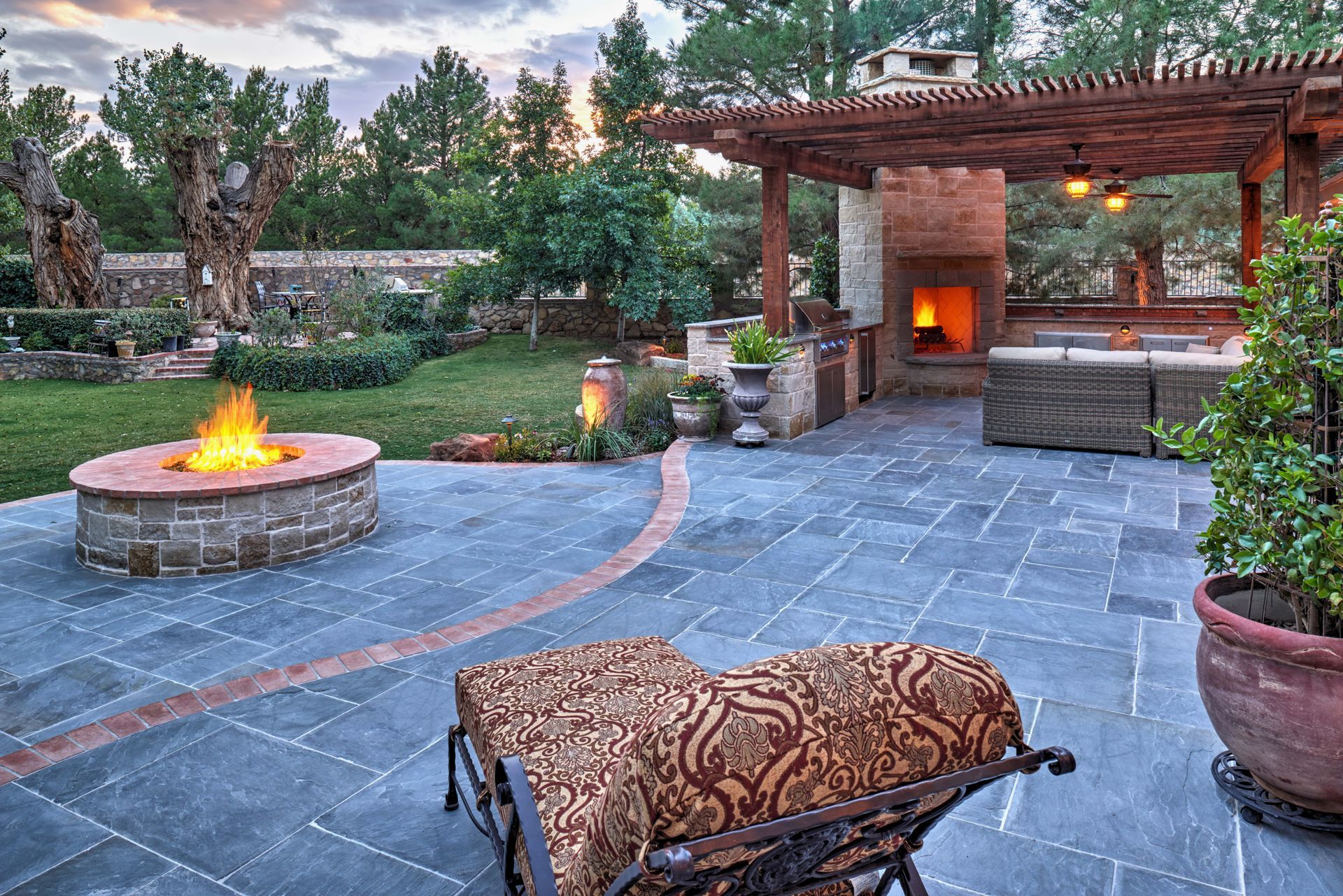 Outdoor patio with fire pit, fireplace, and lounge seating; brick and stone construction, warm lighting.
