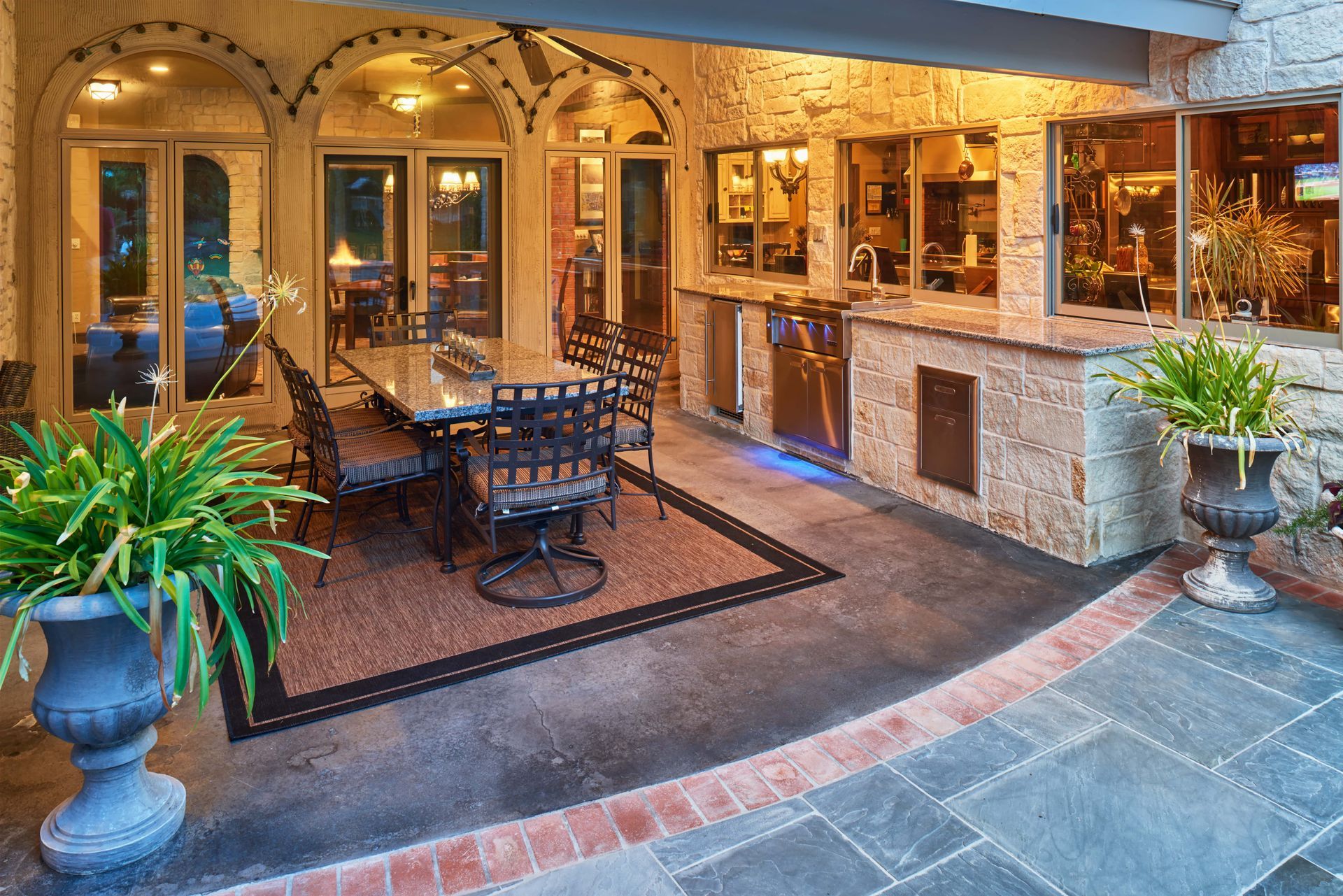 Patio with outdoor dining table, grill, and potted plants, under an archway.