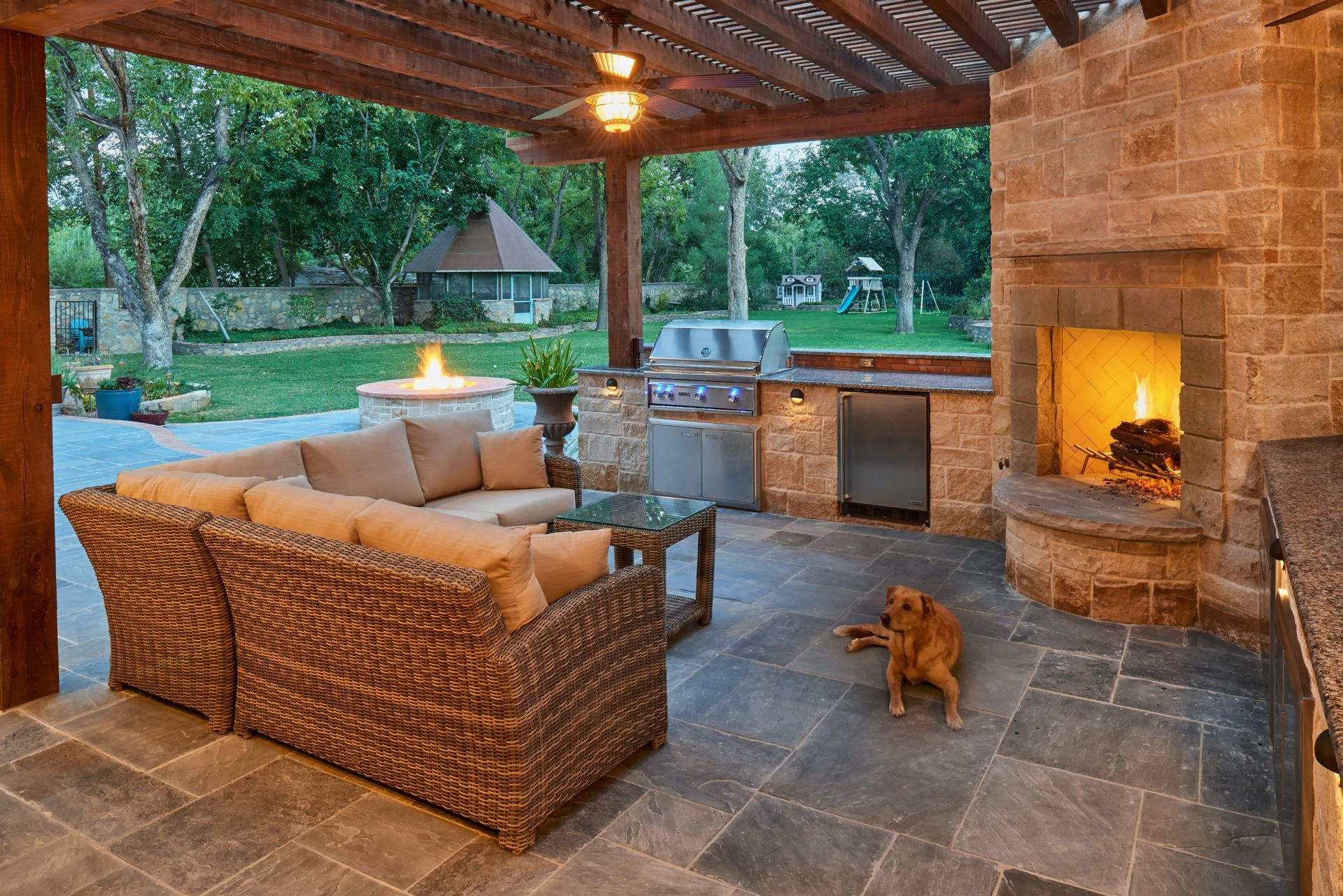 Outdoor patio with seating, fireplace, grill, dog, and pergola.