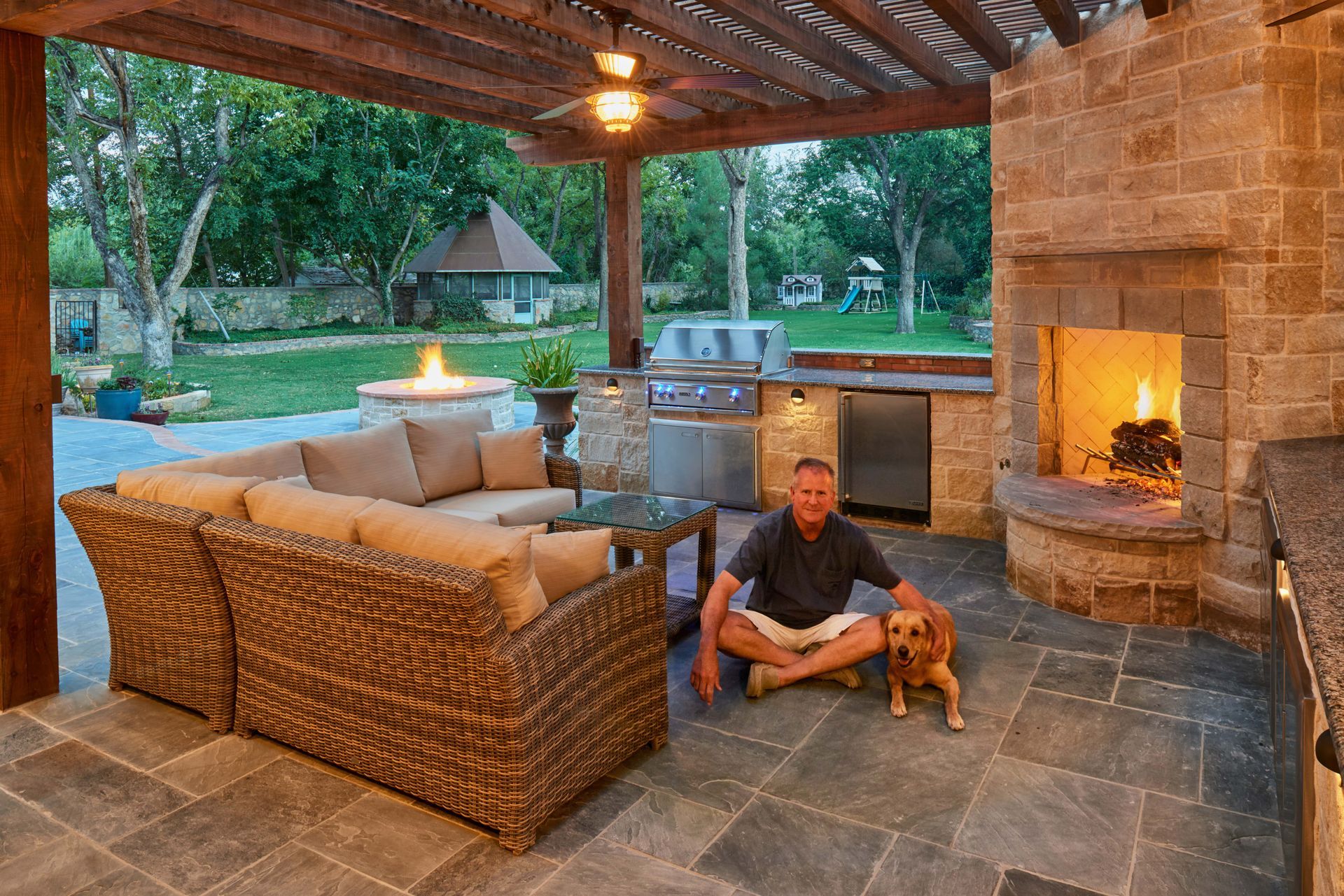 Man and dog on patio with outdoor fireplace, kitchen, and seating area.