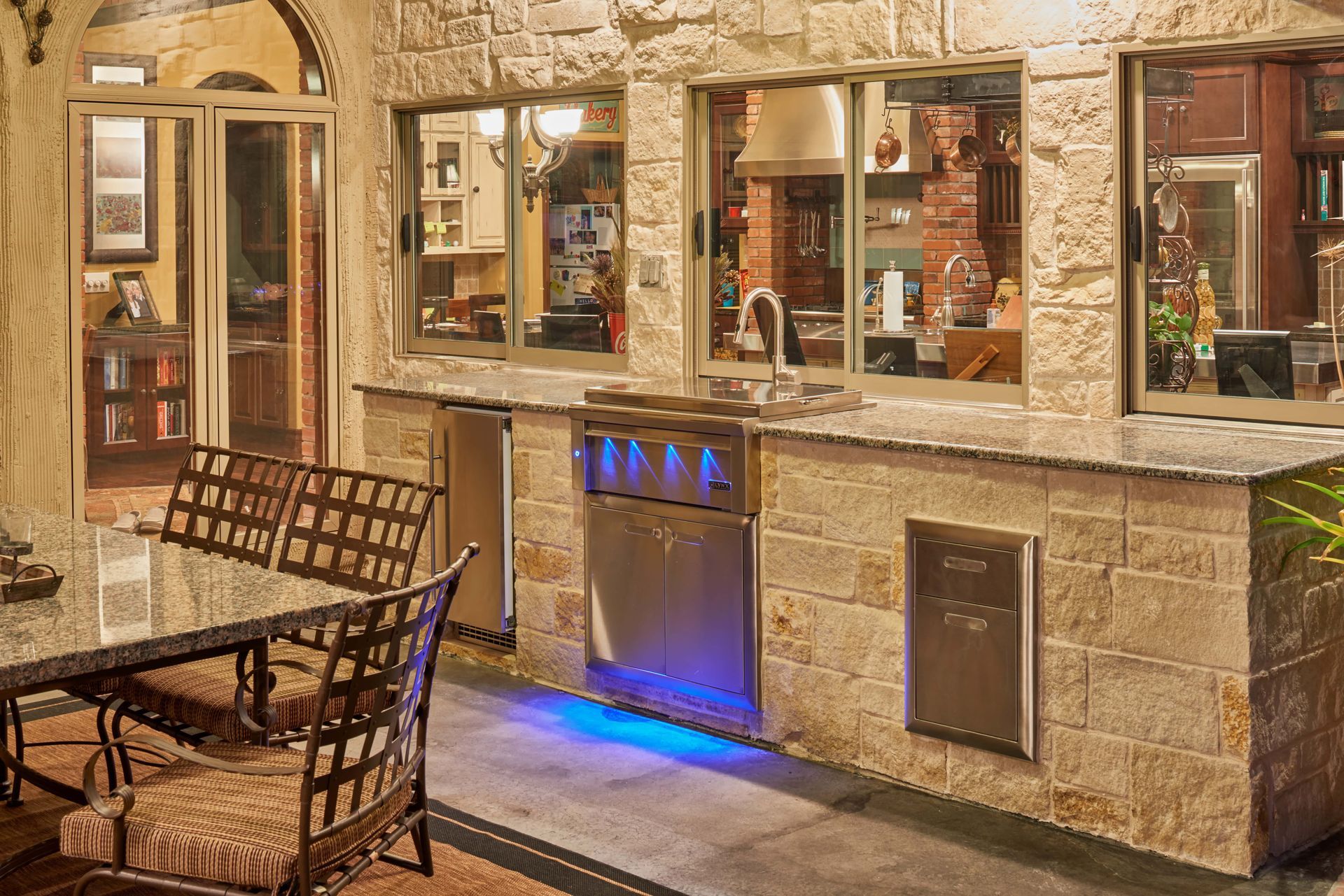Outdoor kitchen with stainless steel appliances, stone counter, and dining table.