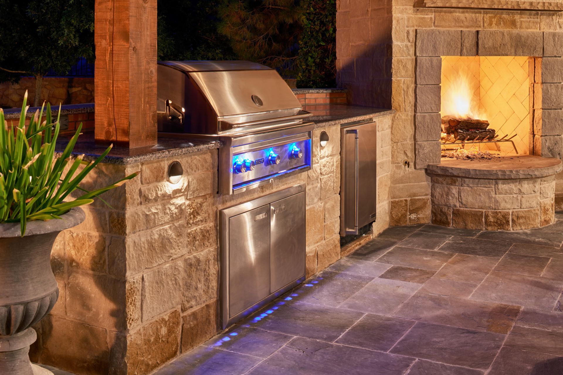 Outdoor kitchen with grill, refrigerator, and fireplace, built into a stone structure.
