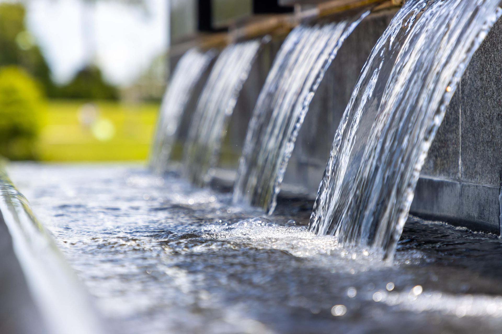Water cascading from a fountain with blurred green background.