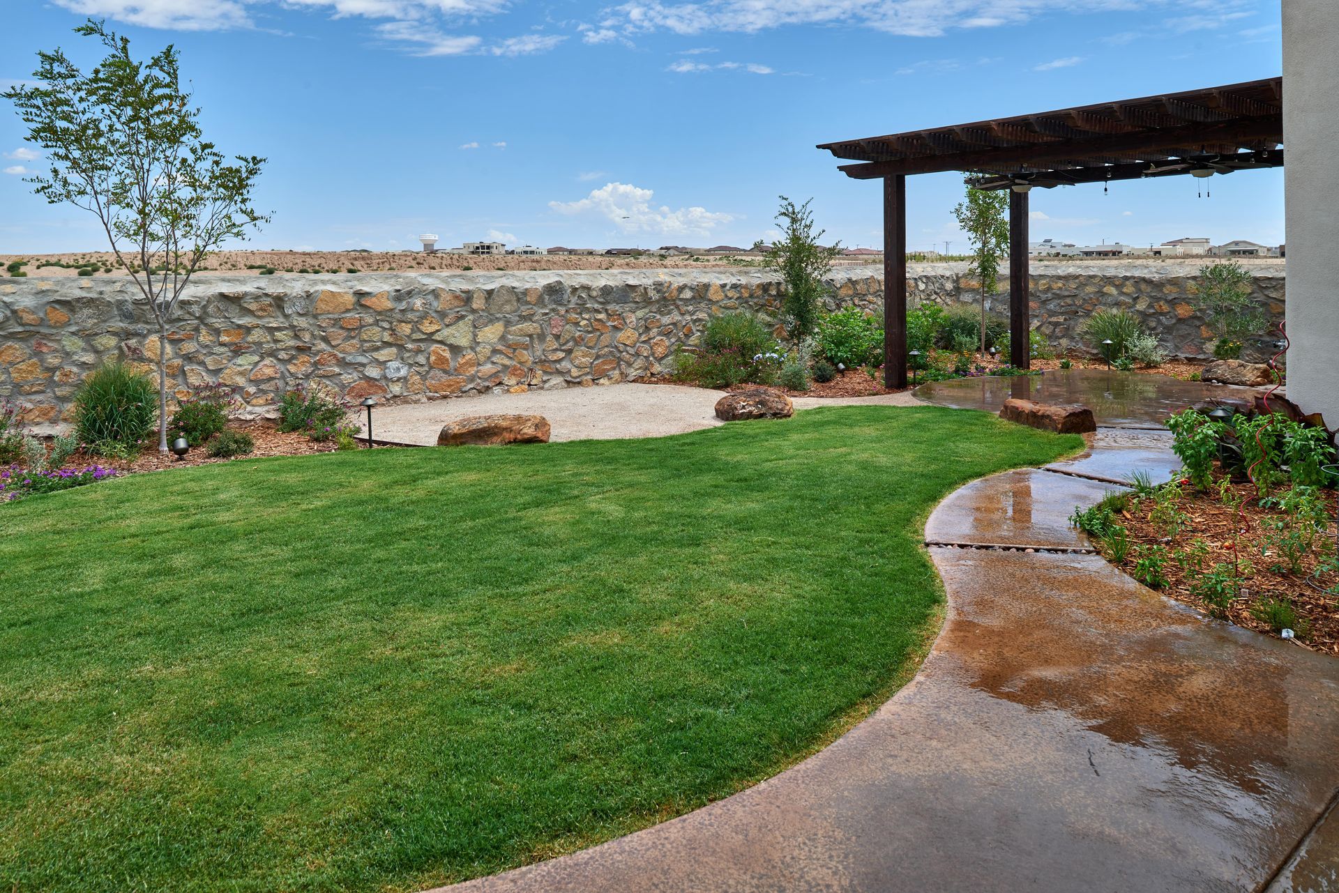 Green lawn, stone wall, and pergola in a sunny outdoor setting with a blue sky.