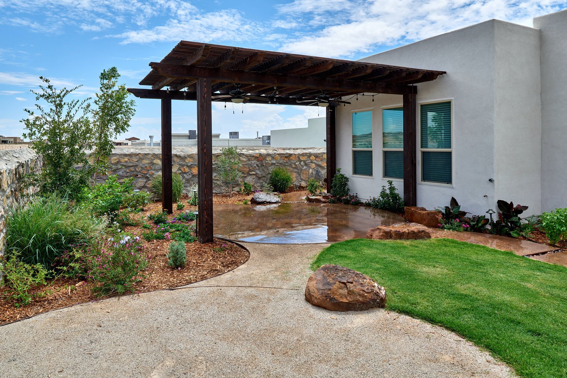 Pergola with stone path, greenery, and small rocks near a building with windows.