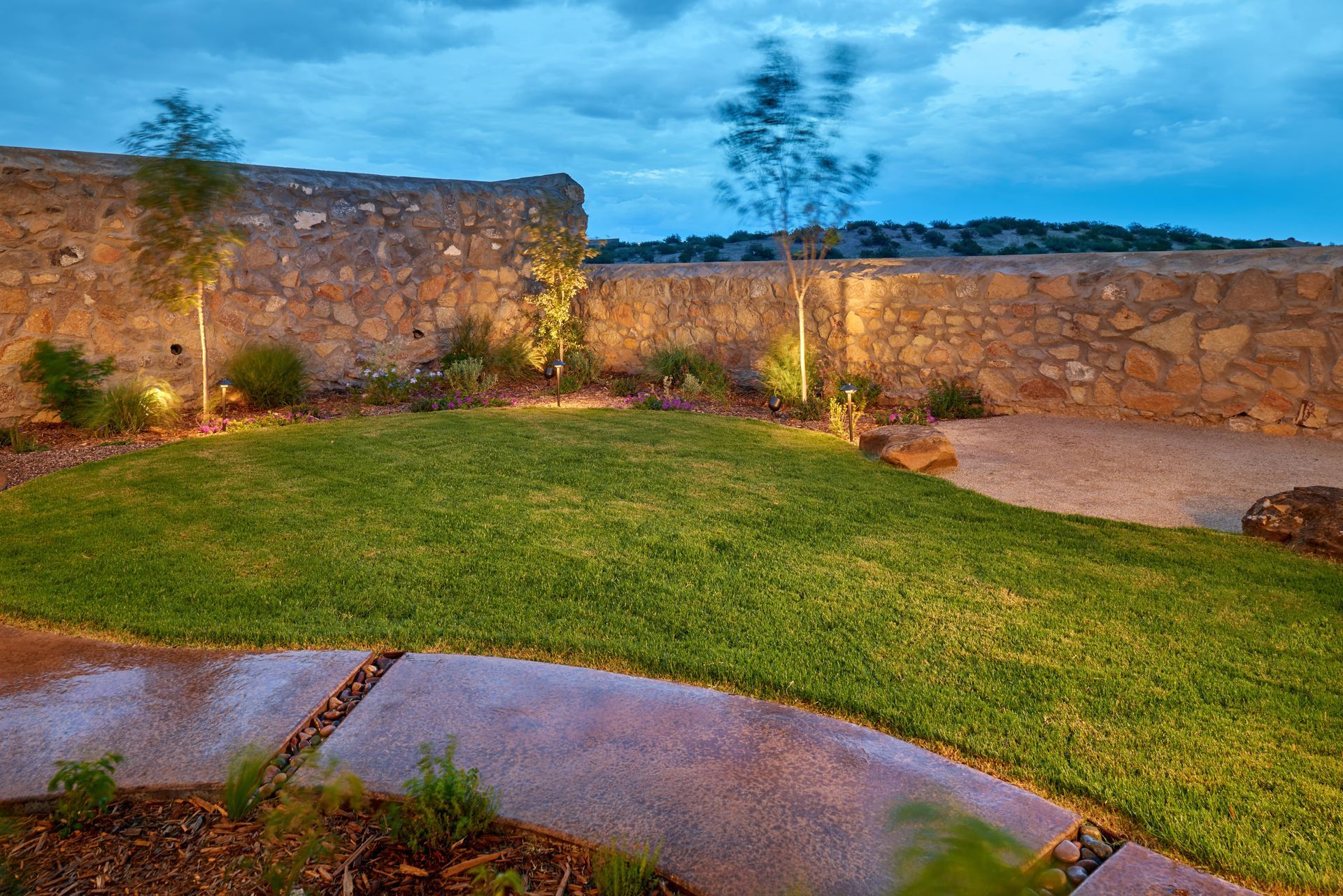 Green lawn in a courtyard with a stone wall and small trees. Overcast sky.
