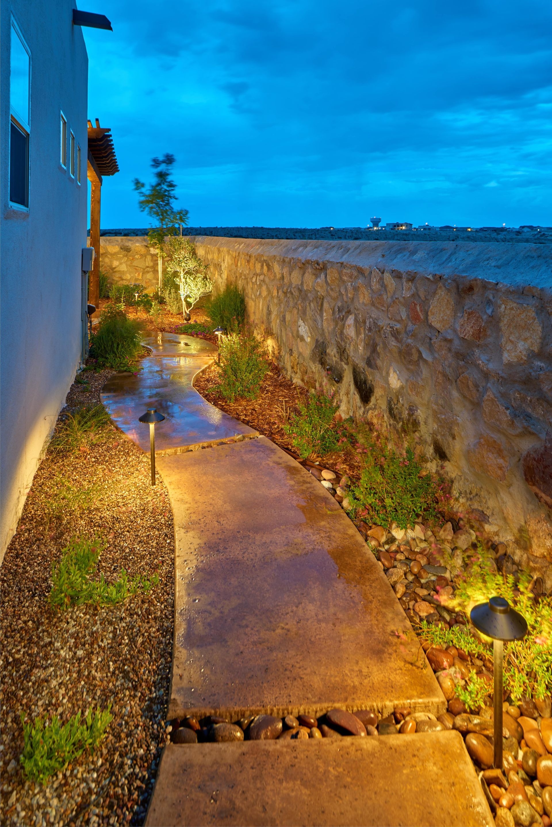 Pathway with low lights and stone wall at dusk.
