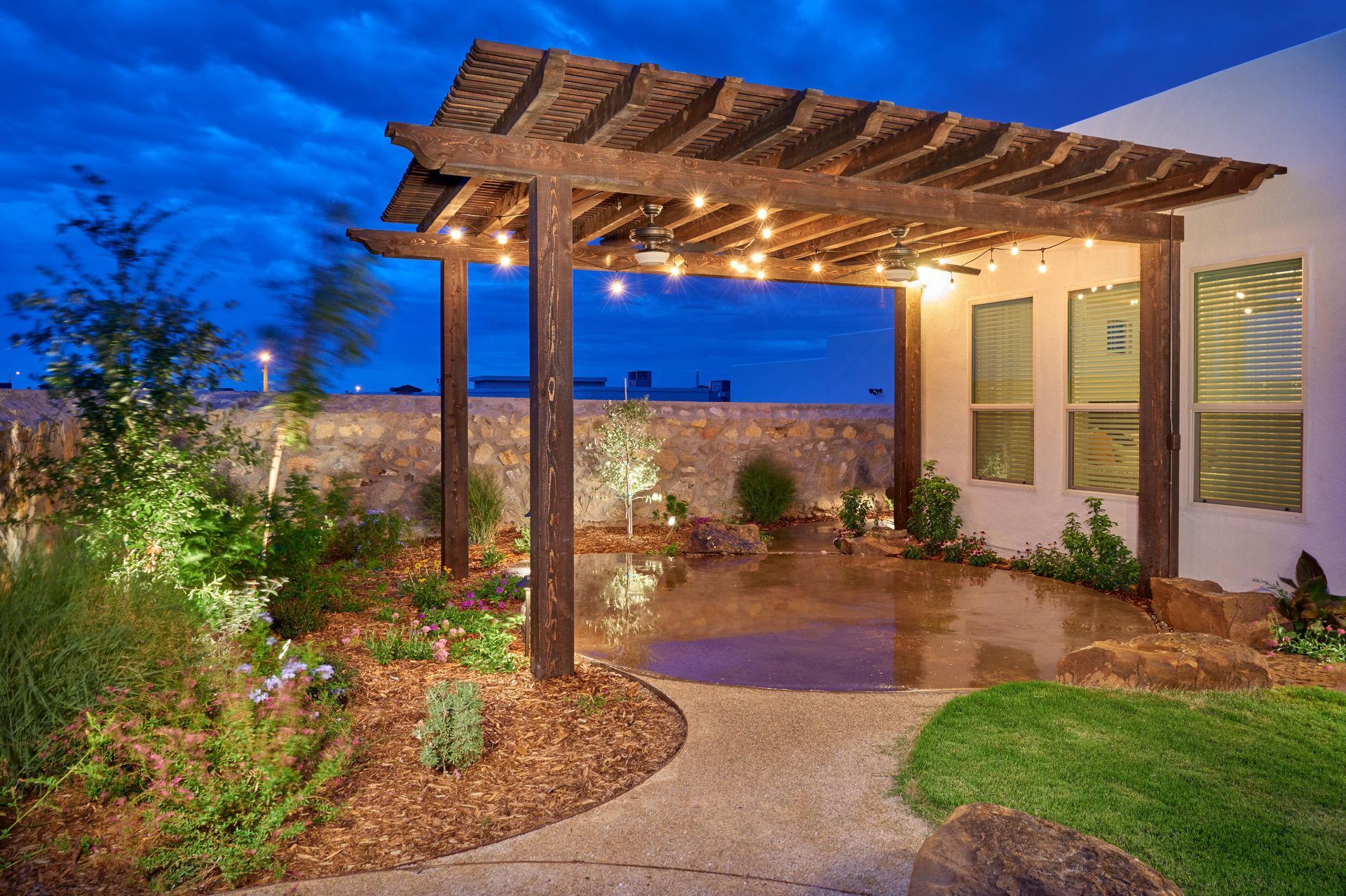 Outdoor patio with wooden pergola, string lights, landscaping, and a cloudy night sky.
