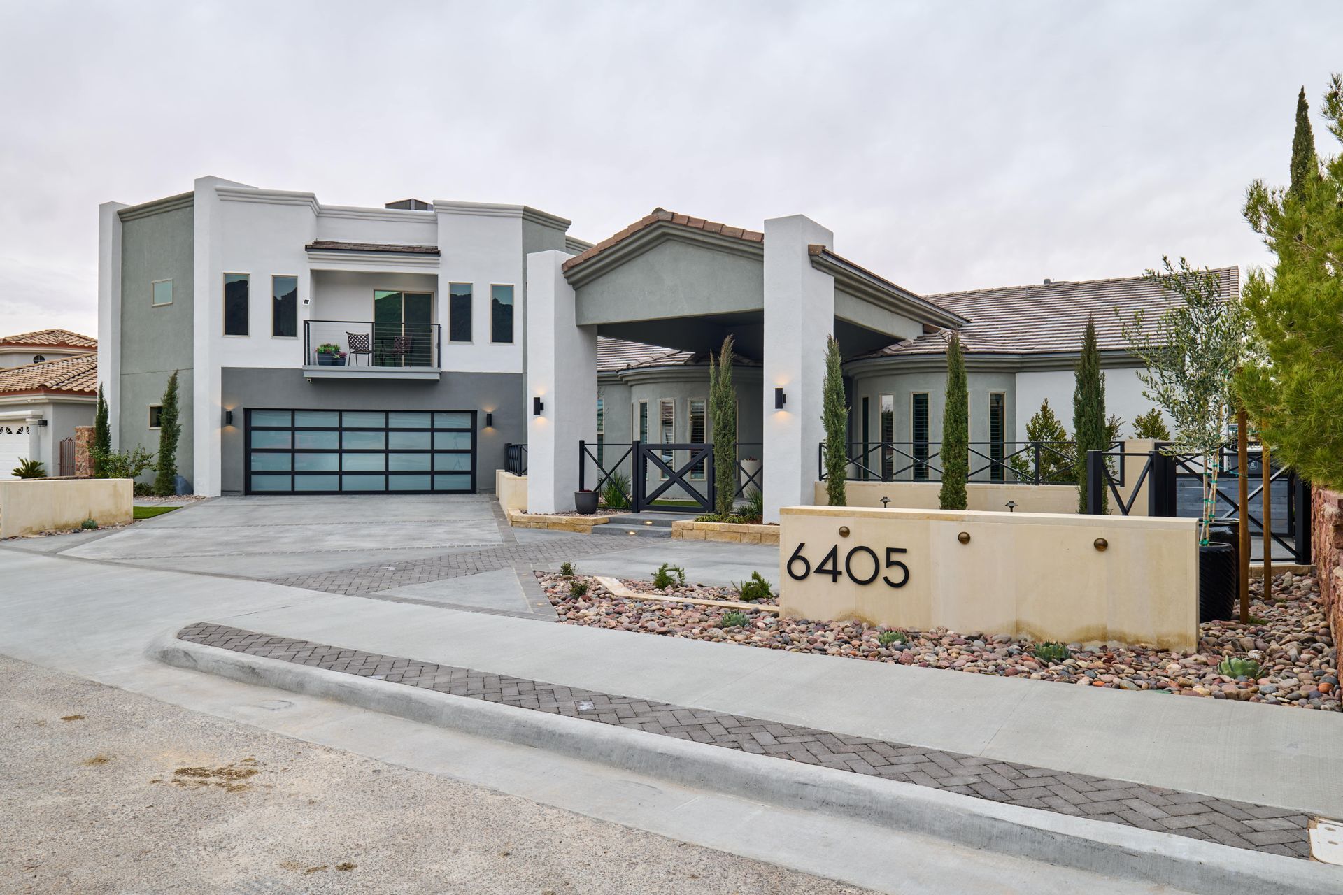 Modern two-story house with a black garage door and address number 6405 on a landscaped driveway.