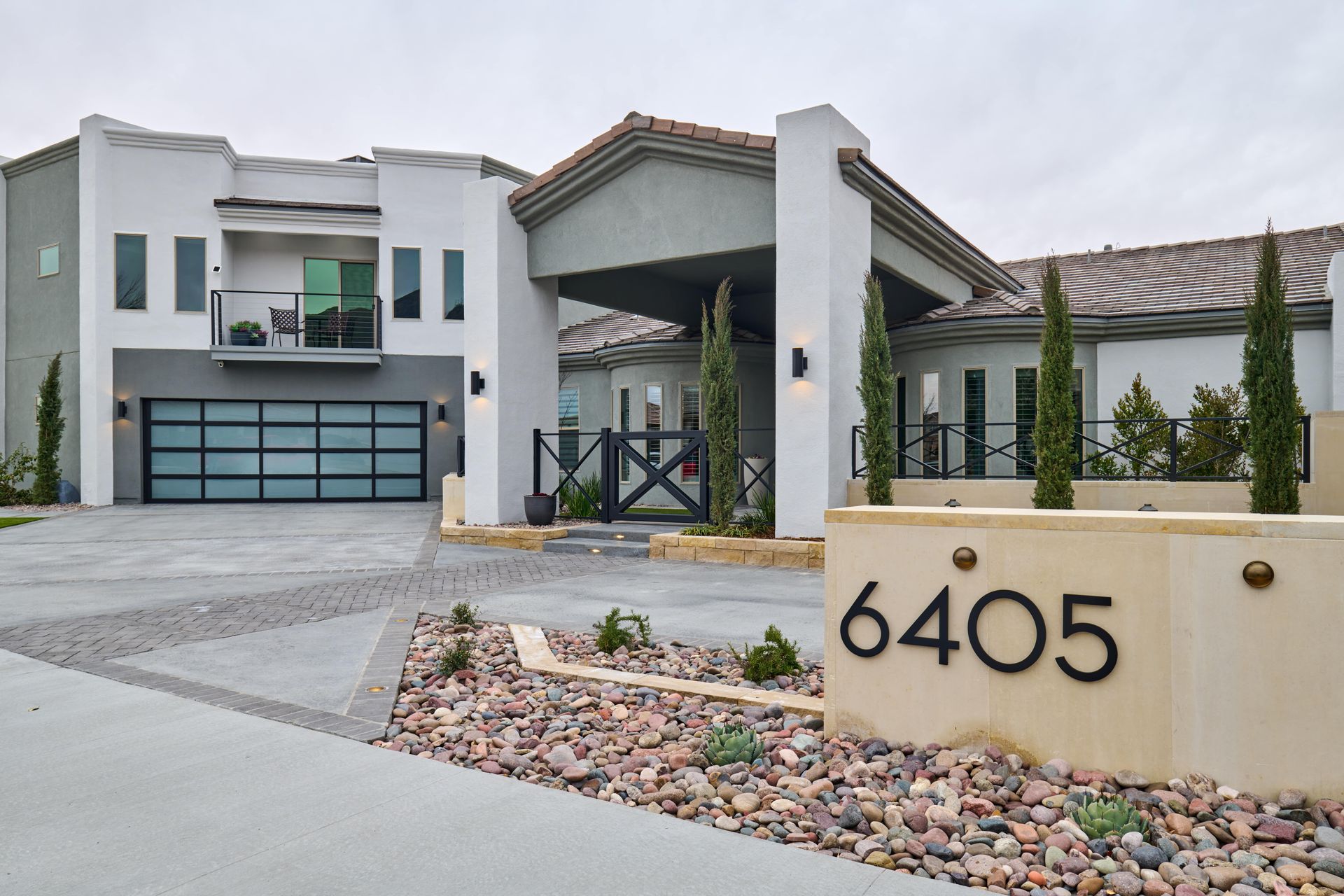 Modern two-story house with gray and white exterior. Features include a glass garage door and a decorative address sign.