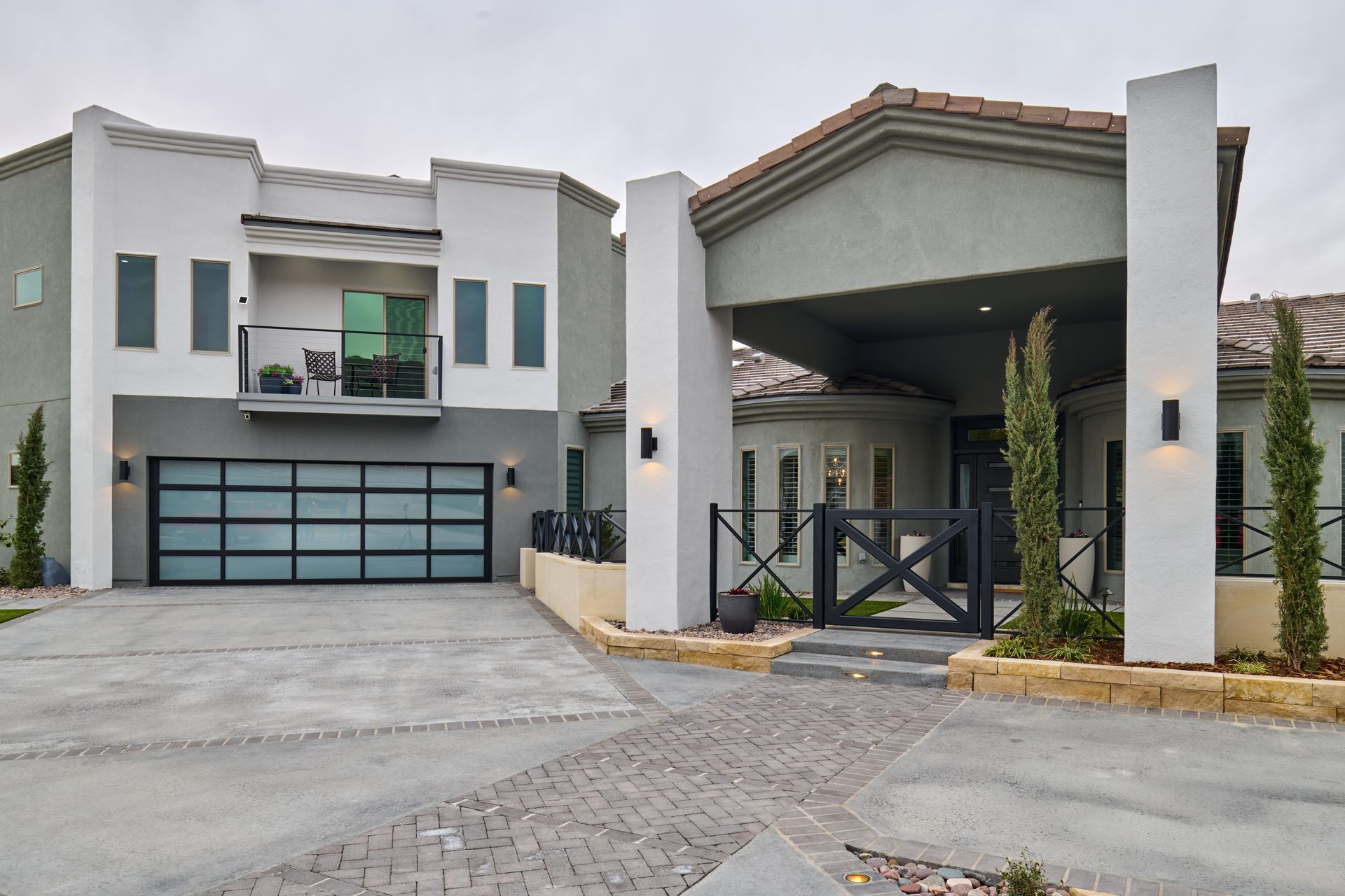 Modern two-story house with a glass garage door, balcony, and covered entrance, gray and white exterior.