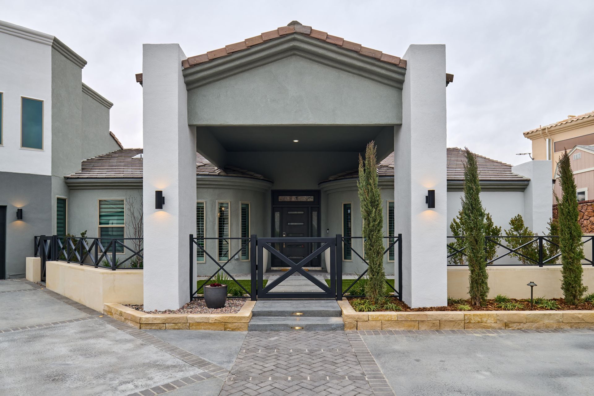 A modern house with a gray exterior, black gate, and landscaping on a stone driveway.