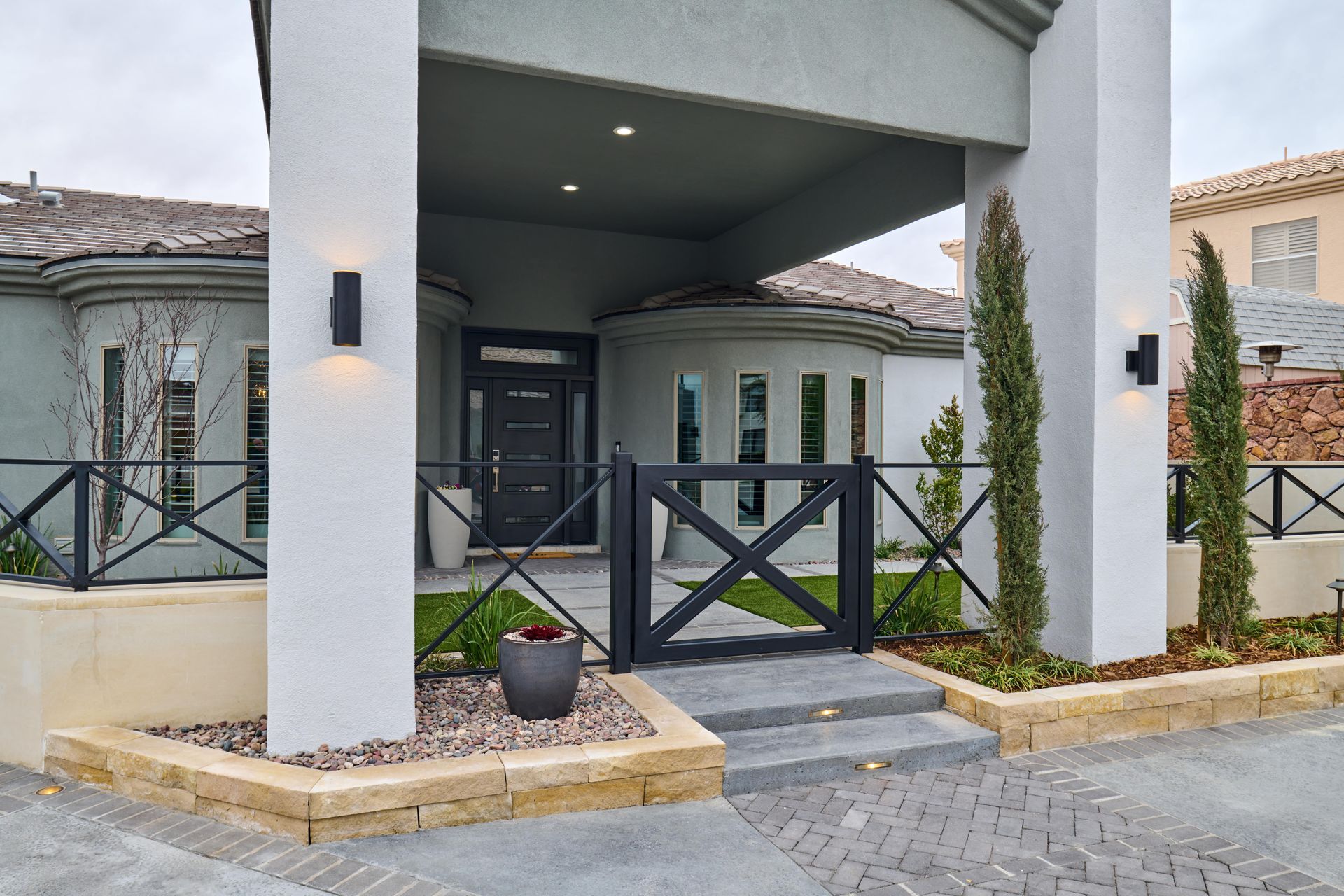Exterior of a home with a black door, gray walls, and a black gate. Two tall columns support the entrance.