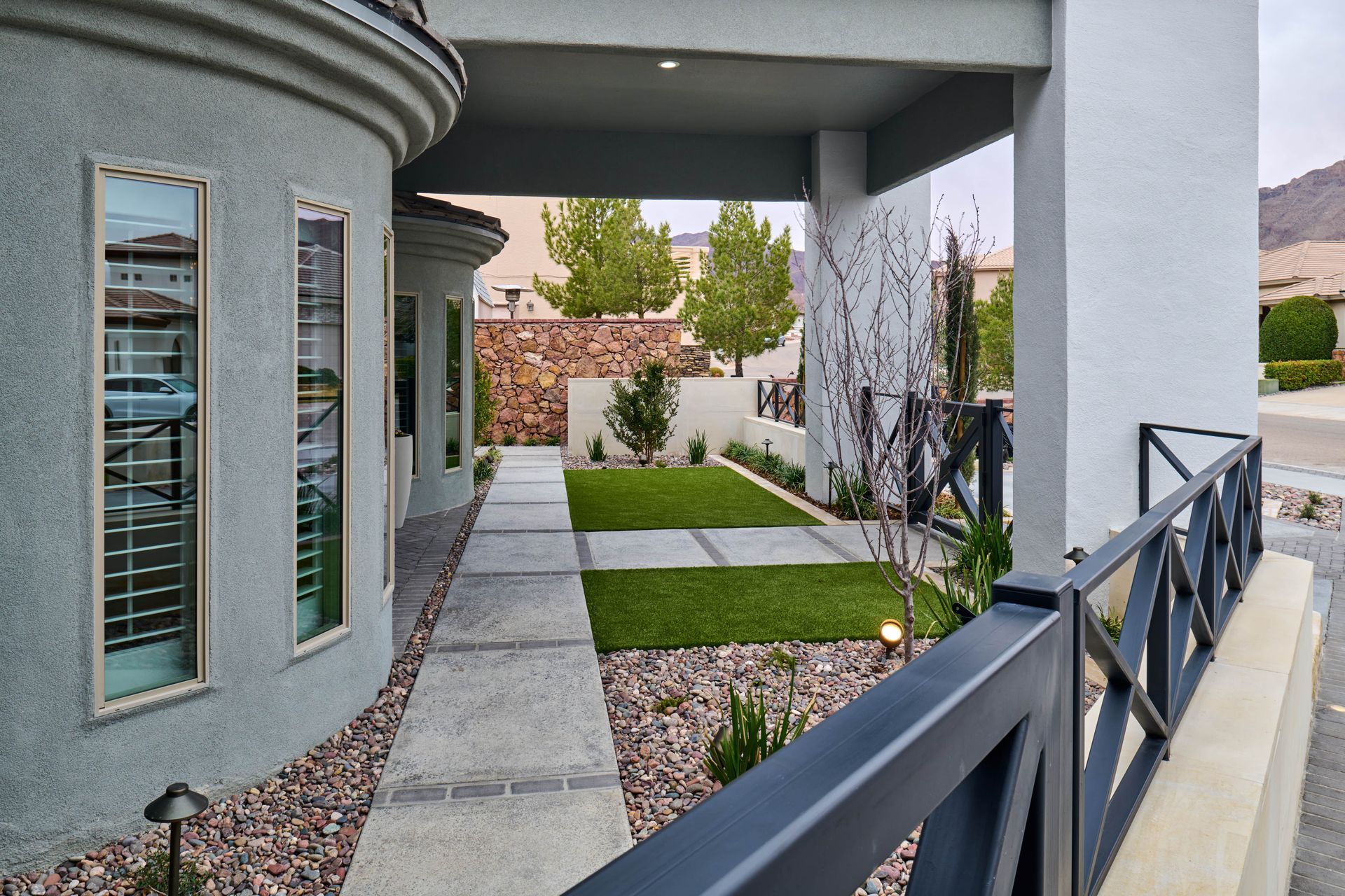 Exterior of a house with a walkway, featuring a fenced patio, windows, and landscaping.