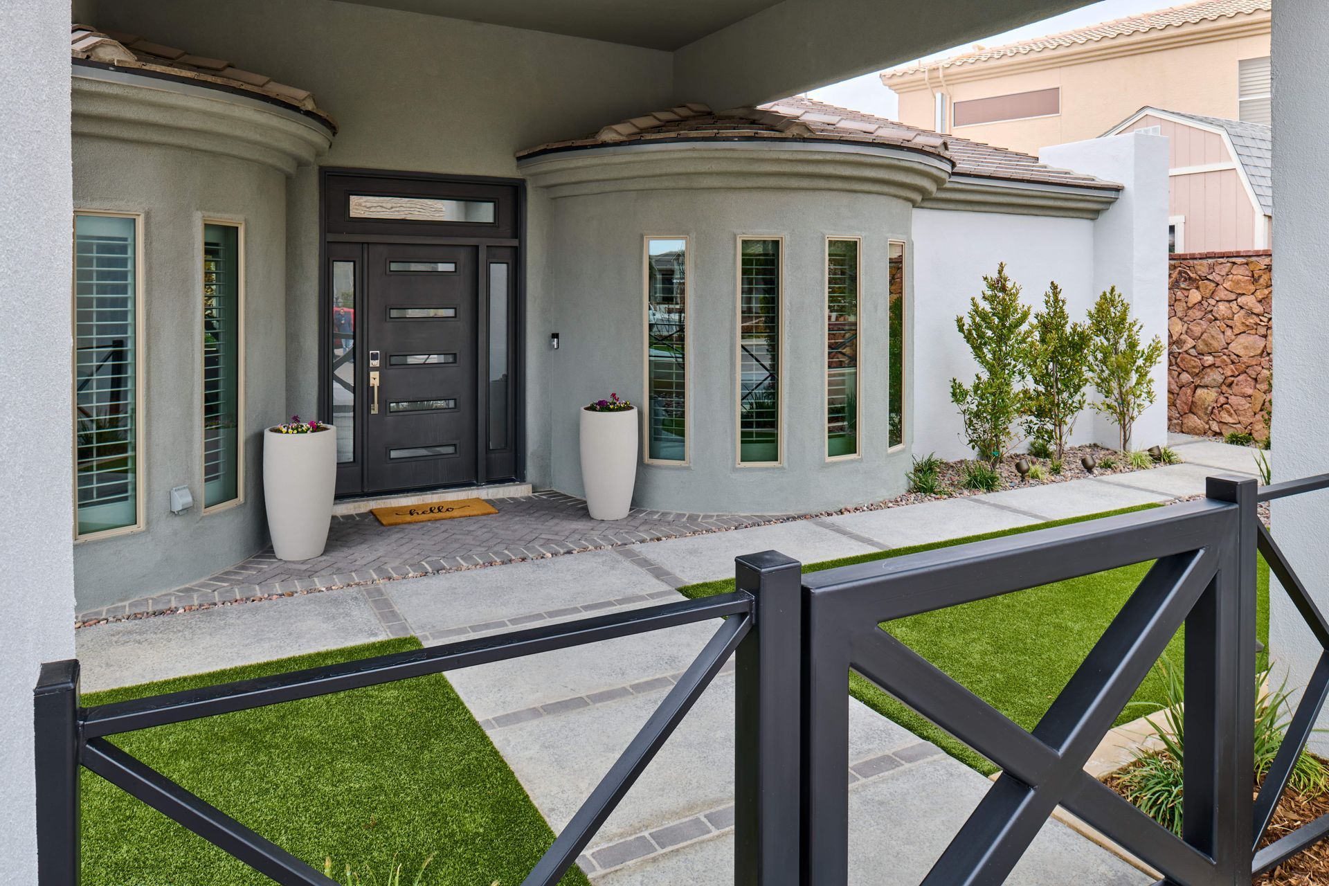 Modern home exterior with gray facade, arched windows, dark front door, and a black fence.