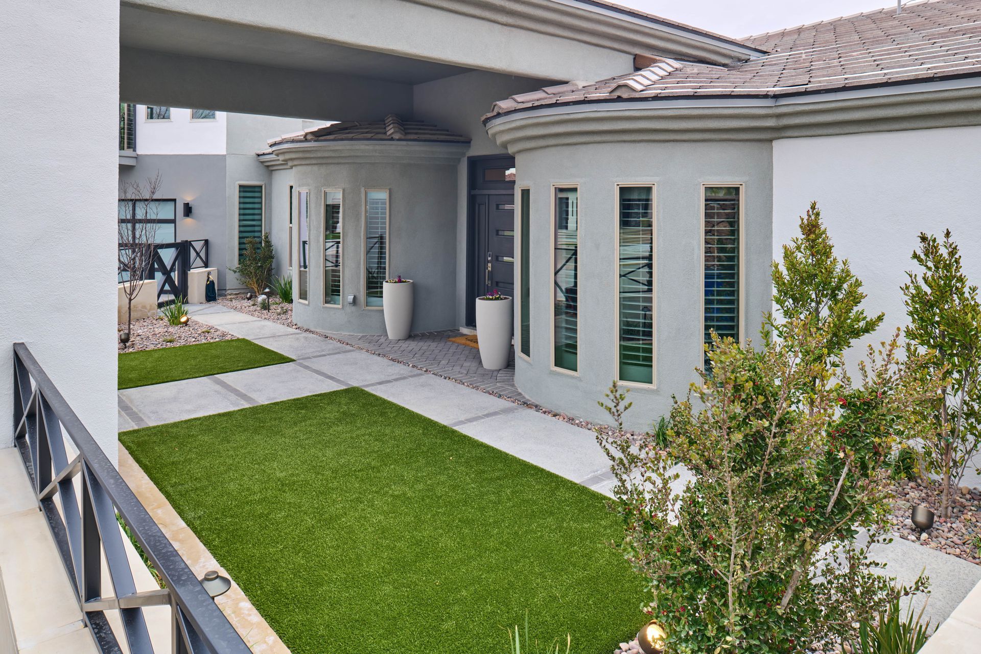 Exterior of a modern house with a green lawn, concrete path, and arched entryways in a cloudy setting.
