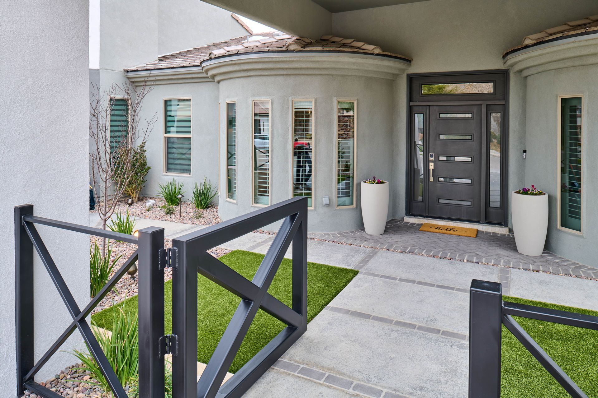 Gray home exterior with modern black door, gate, and landscaping.