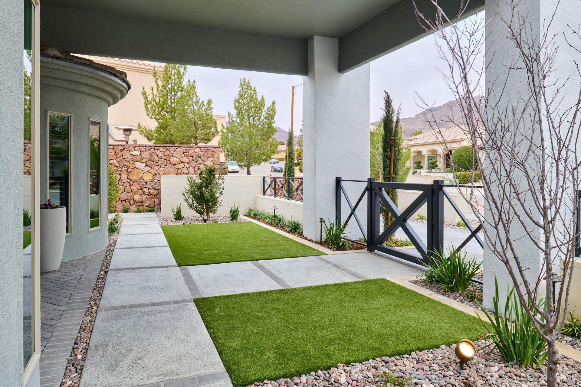 Outdoor covered walkway with concrete pavers, artificial turf, and a small black gate.