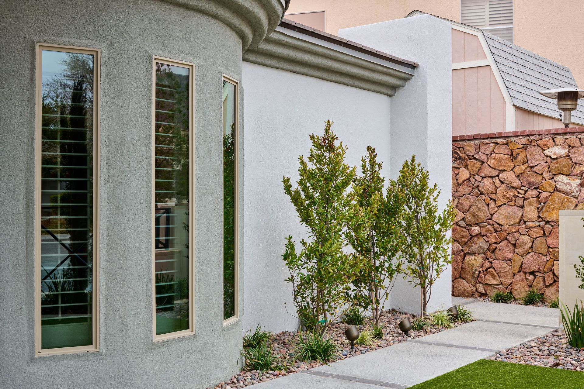 Exterior of a modern home with tall, narrow windows, stucco walls, and a stone accent wall.