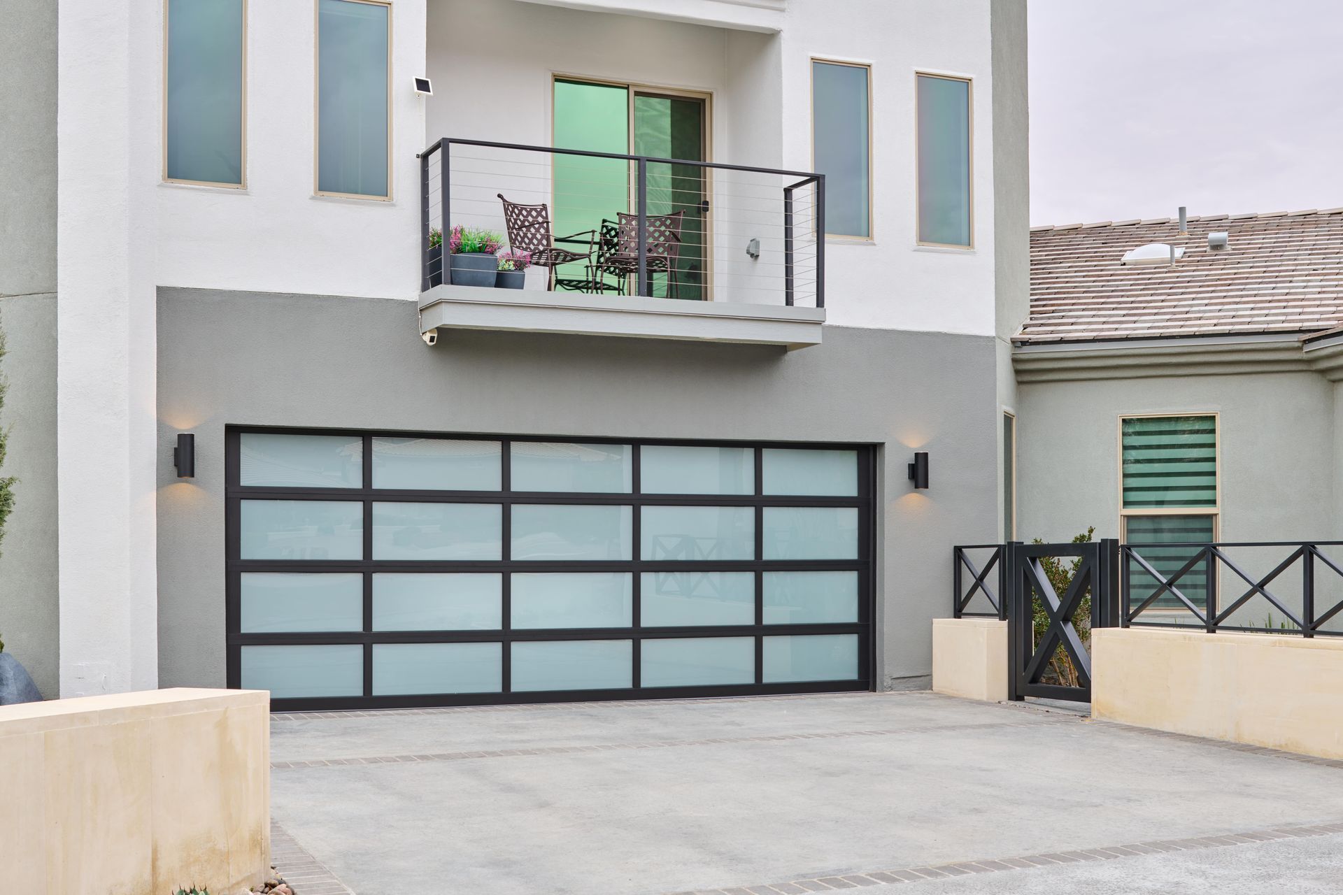 Modern two-story house with a garage and balcony. Frosted glass garage door, gray and white exterior.