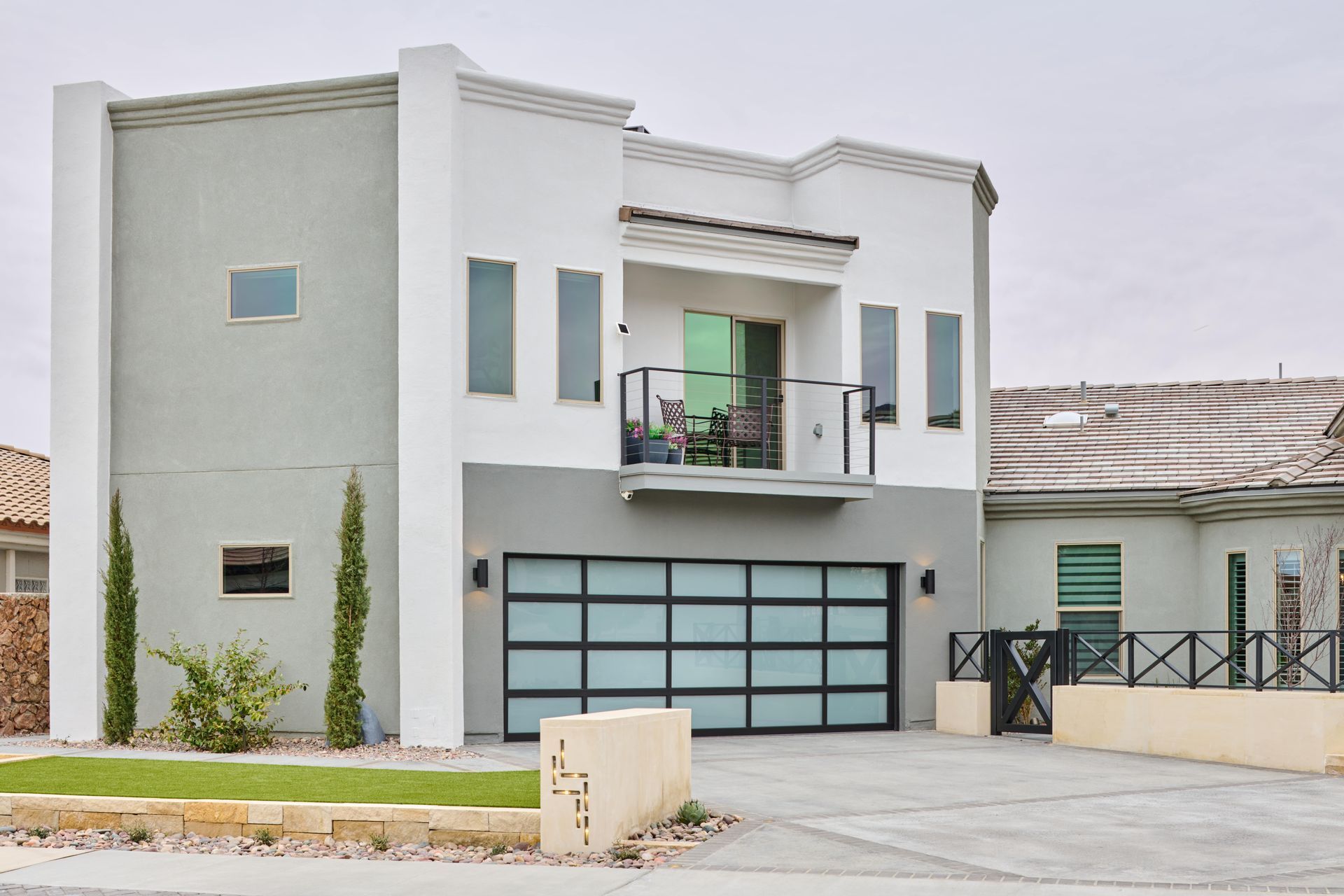 Modern two-story house with gray and white facade, glass garage door, and small balcony.