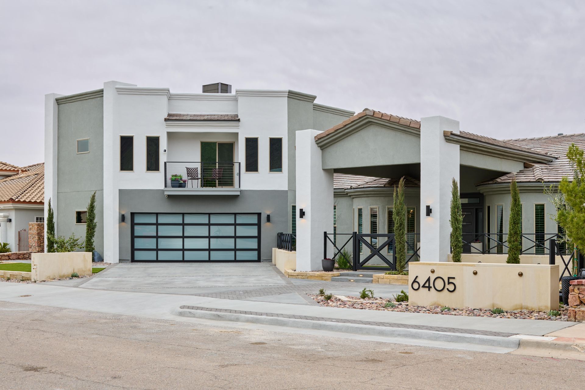 Modern two-story house with gray and white exterior, a glass garage door, and a covered entryway.