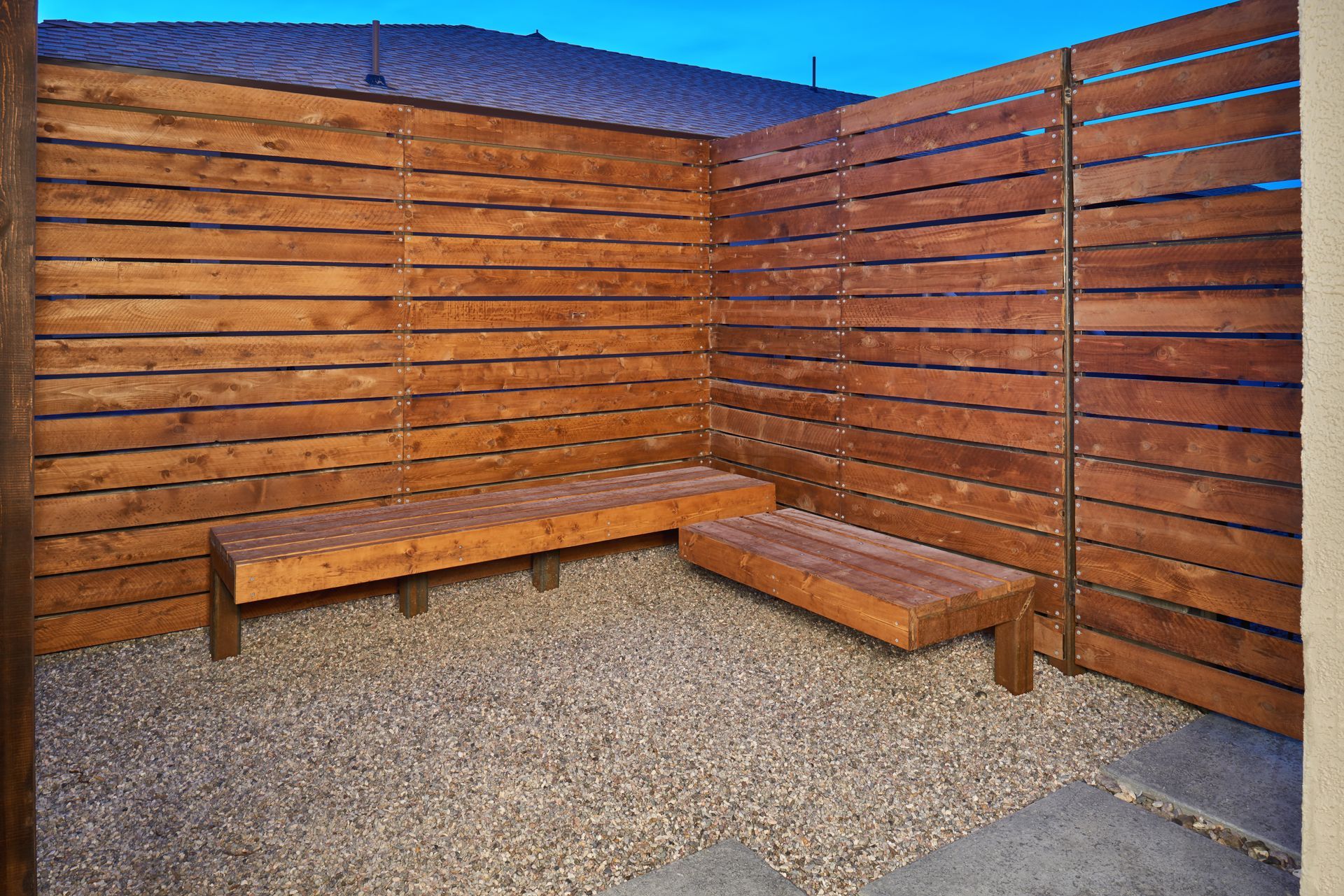 Wooden benches in a small, fenced, gravel-covered outdoor space.