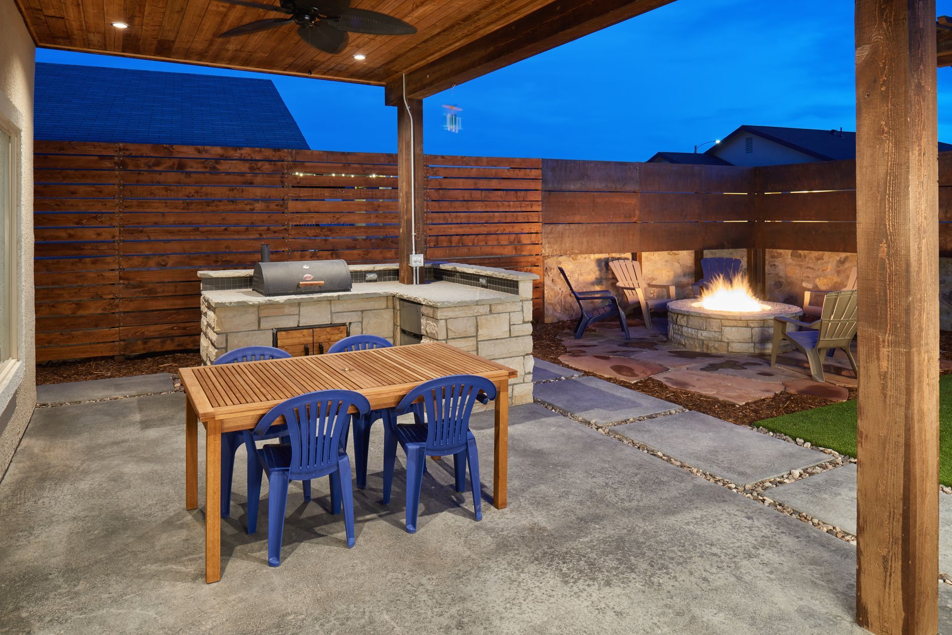 Outdoor patio with grill, dining table, fire pit, and wooden fence.