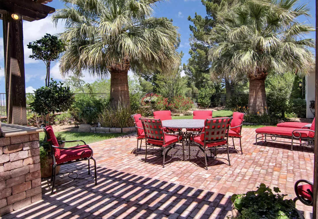 Outdoor patio with red brick and furniture, palm trees, and sunny blue sky.
