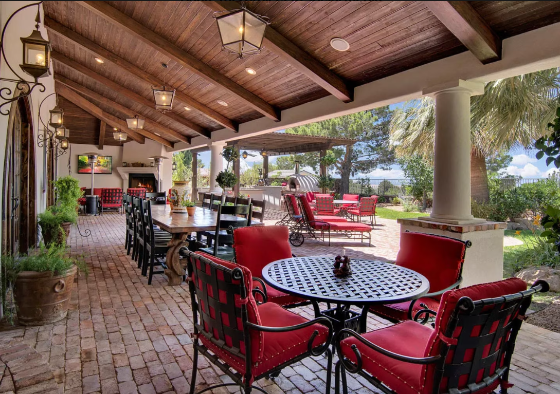 Covered patio with red furniture, long table set for dining, and lush garden views.