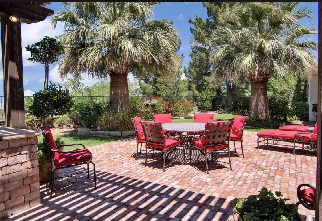 Patio with red chairs, round table, and lounge chairs on brick pavers under palm trees.