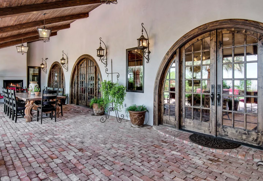 Patio with brick floor, arched wooden doors, dining table, and lanterns.