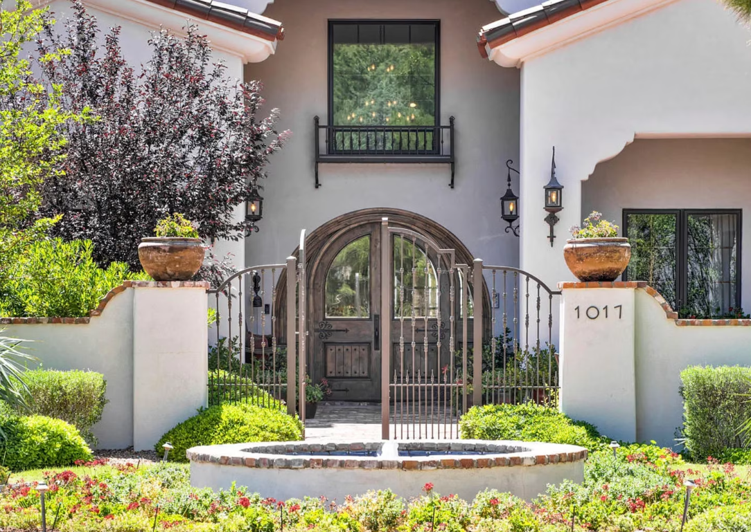 Spanish-style home entrance with arched gate, fountain, and manicured landscaping.