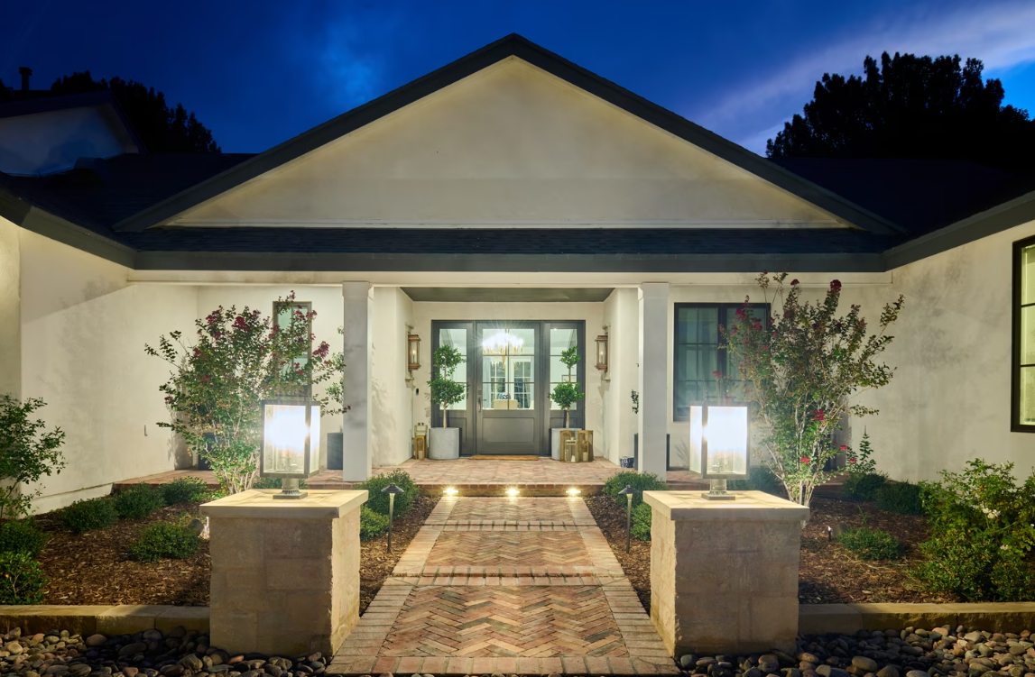 Lit pathway to a home entrance at dusk, with outdoor lights and landscaping.