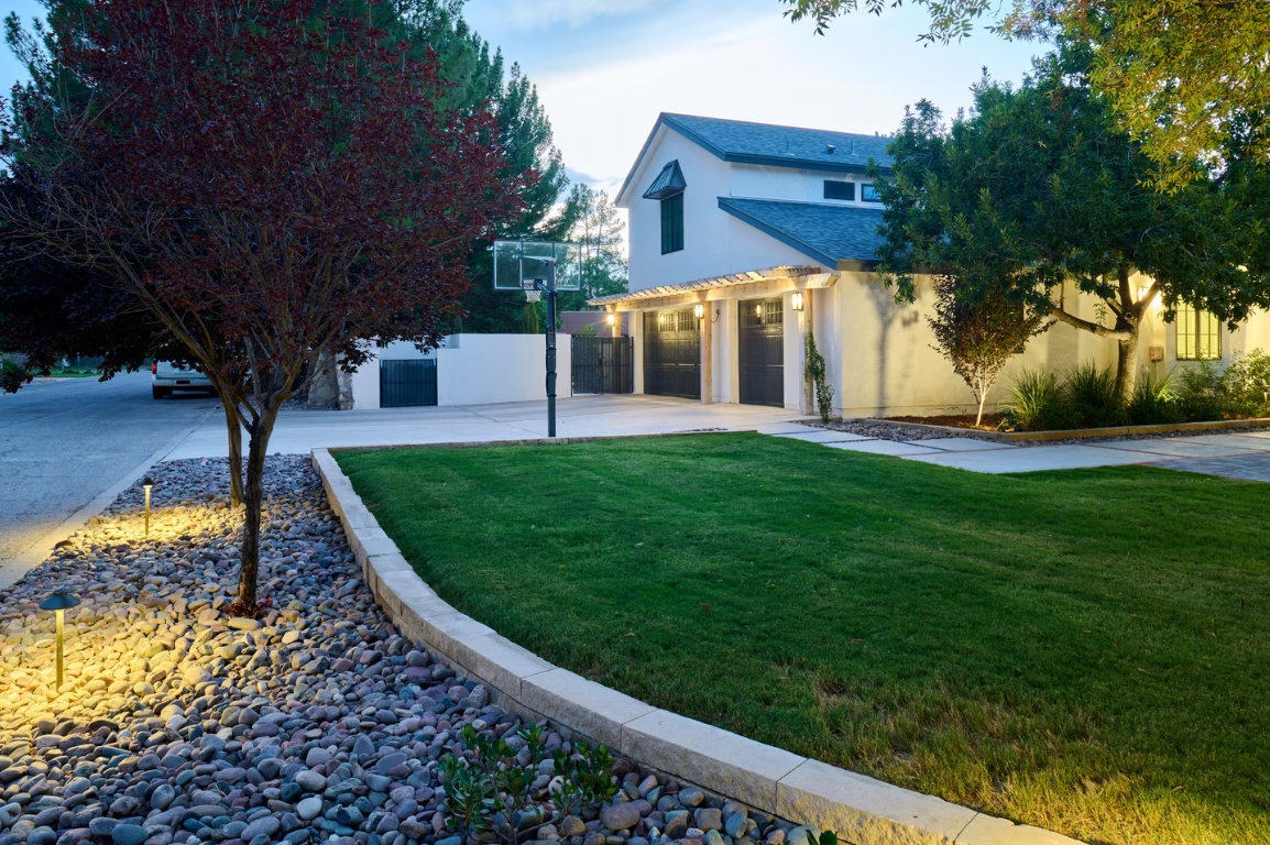 Lush green lawn with a low concrete border, fronting a house with a basketball hoop in the driveway.