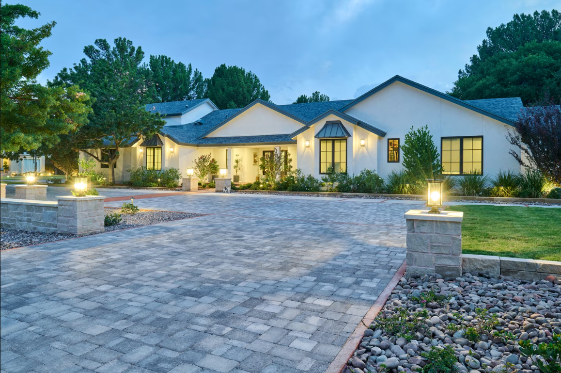 White house with stone driveway and columns, illuminated at dusk.