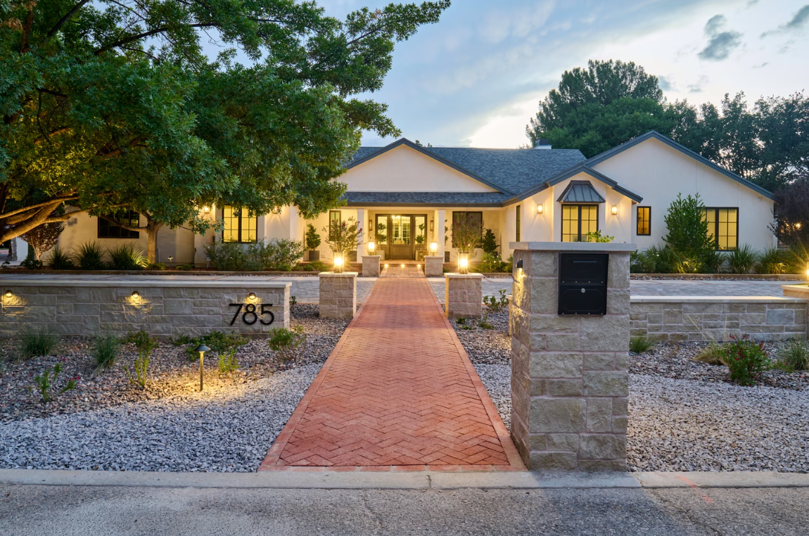 Front exterior of a modern ranch-style home with illuminated pathway, stone accents, and manicured landscaping.